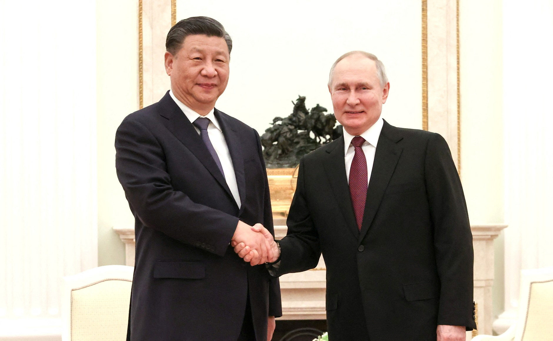 Russian President Vladimir Putin and Chinese President Xi Jinping shake hands while looking at the camera.