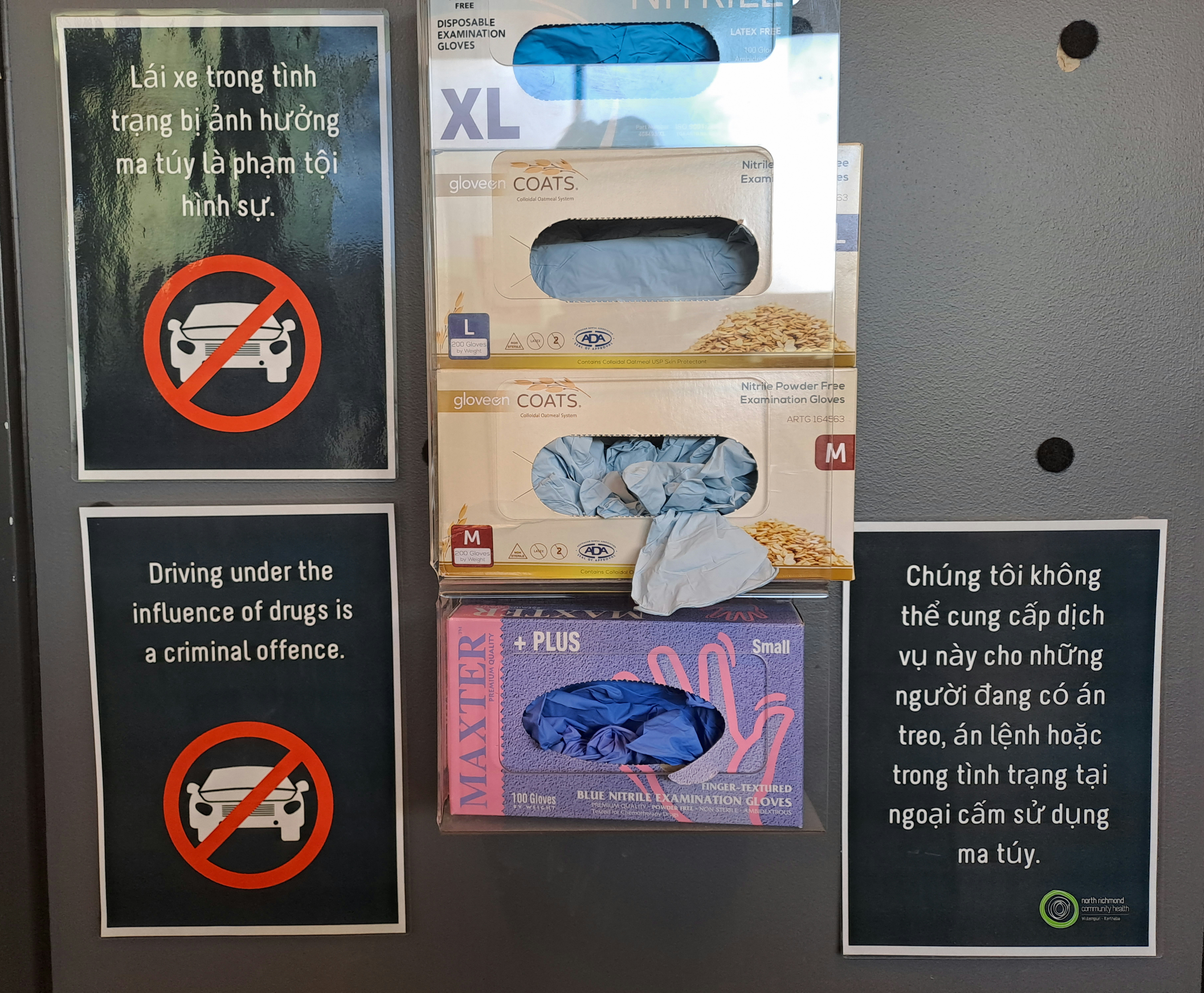 There are three posters on the board. One looks laminated. In between them are boxes of different-sized latex gloves.