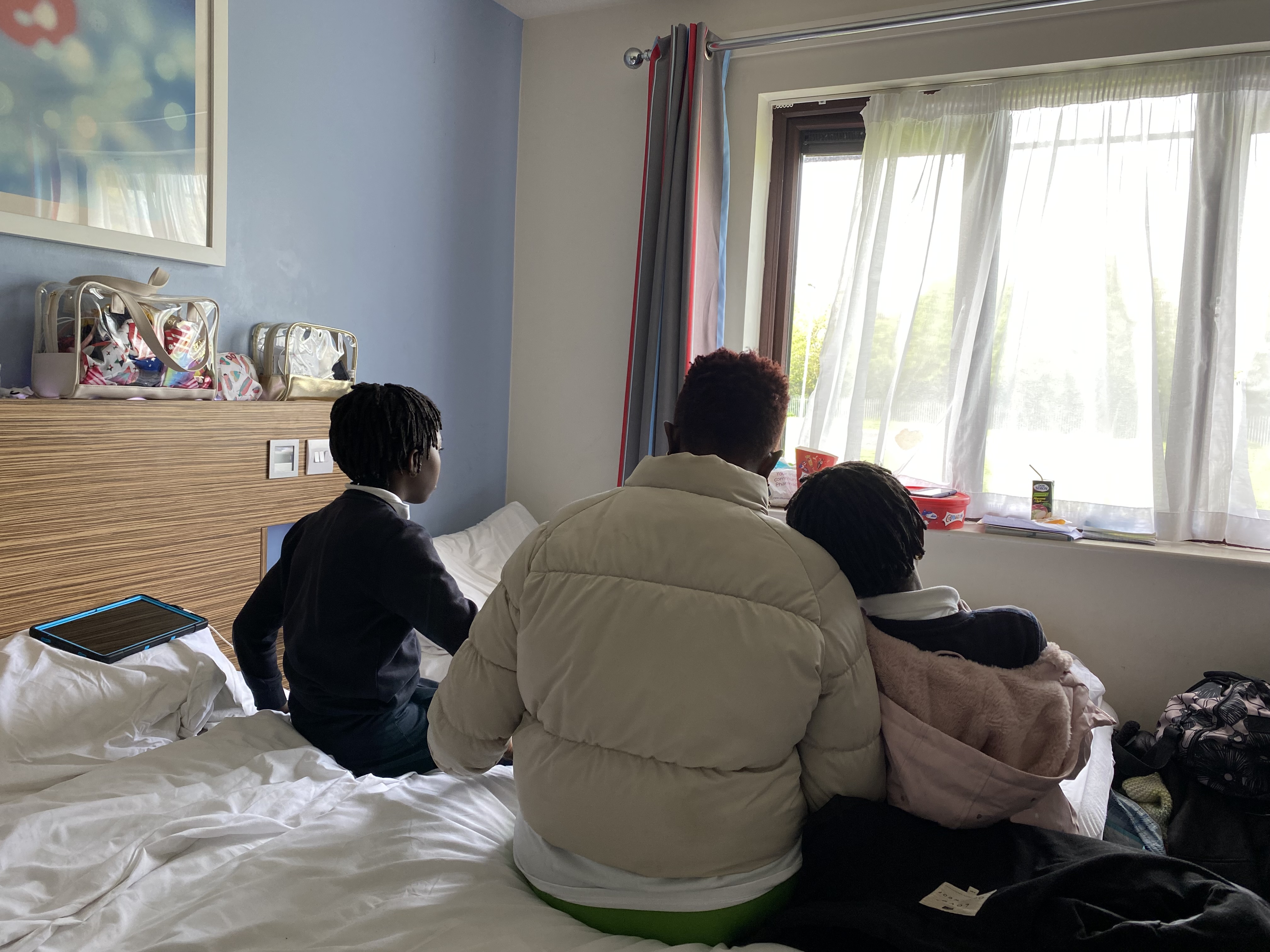 A woman and her two daughters sit on a bed in a room