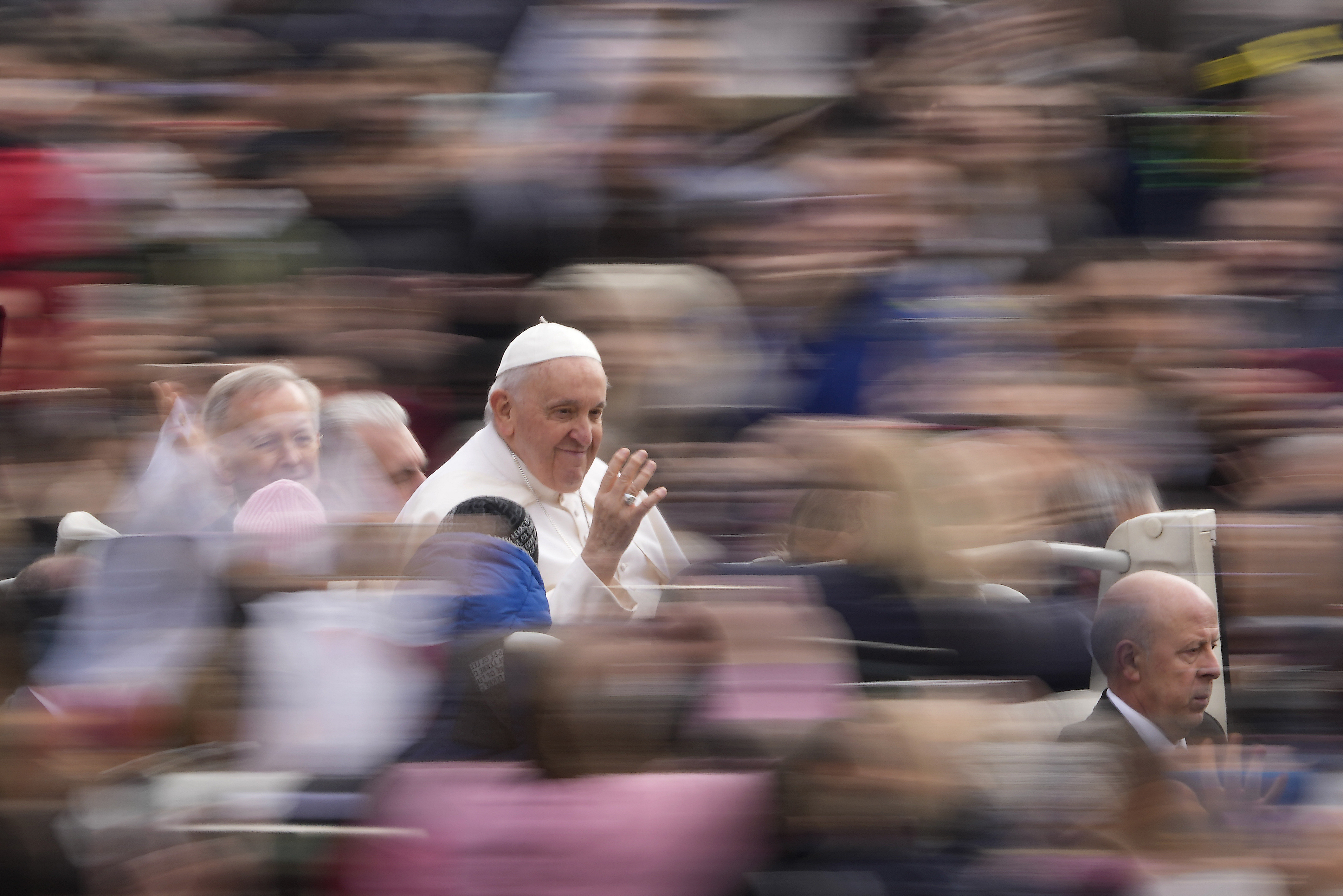The Pope pictured entering St Peter's Square. The crowd around him is blurred. He is waving and smiling.