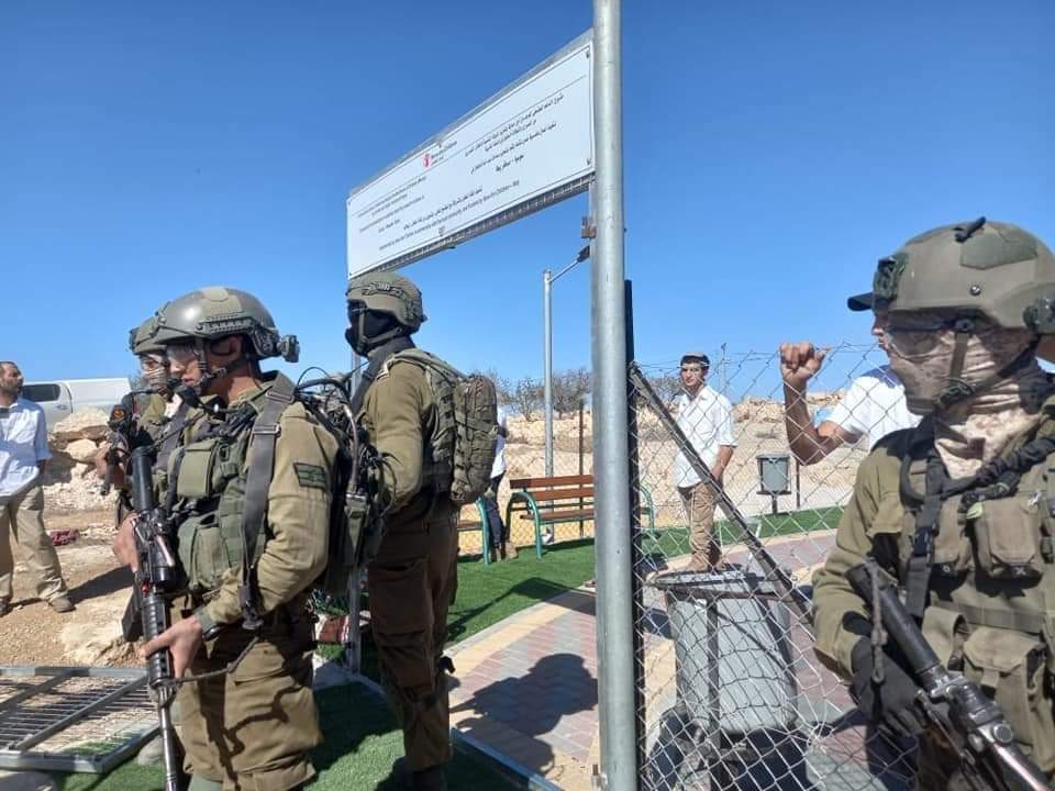 Israeli soldiers stand guard as the Israeli settlers play on Khirbet Susiya’s playground.