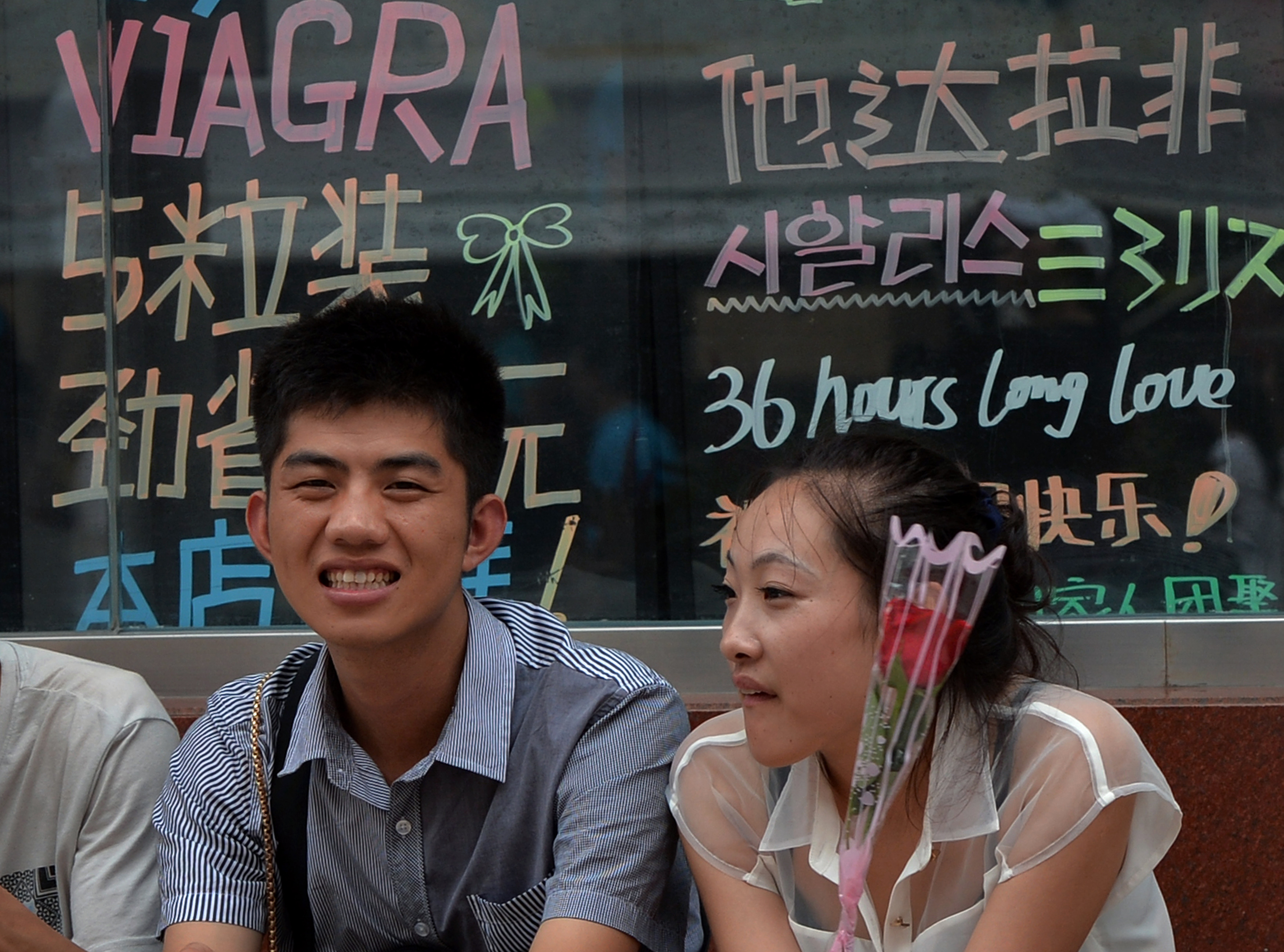A young girl holds a rose next to her boyfriend as they sit beneath a Viagra sign during the Qixi festival which is also known as the 'Chinese Valentine's Day' in Beijing on August 13, 2013. The festival dates back over 2600 years and is a popular and auspicious wedding date for Chinese couples. AFP PHOTO/Mark RALSTON