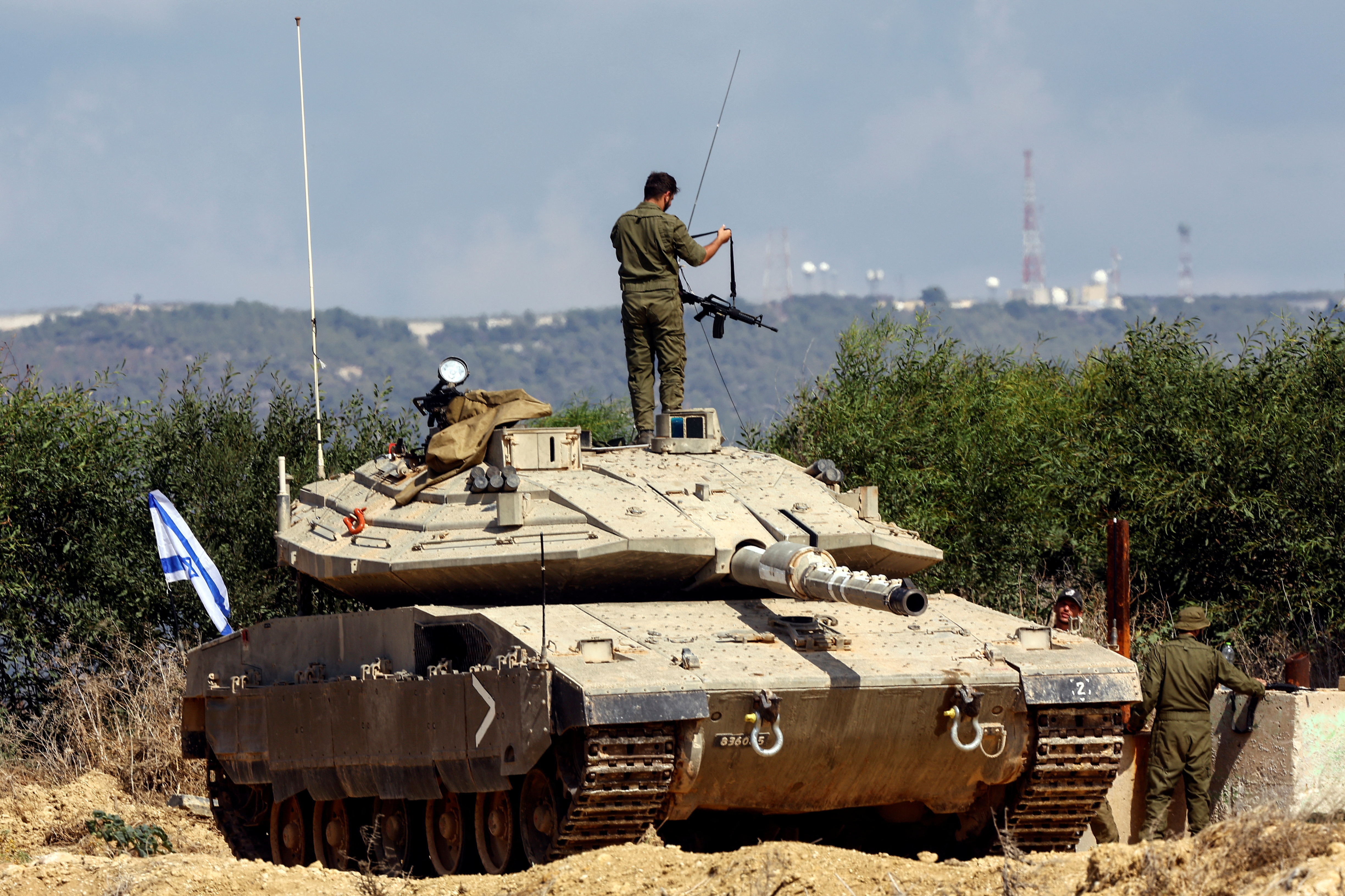 An Israeli soldier holds a rifle by its strap as he adjusts it, while standing atop a tank in Israel's northern border region.