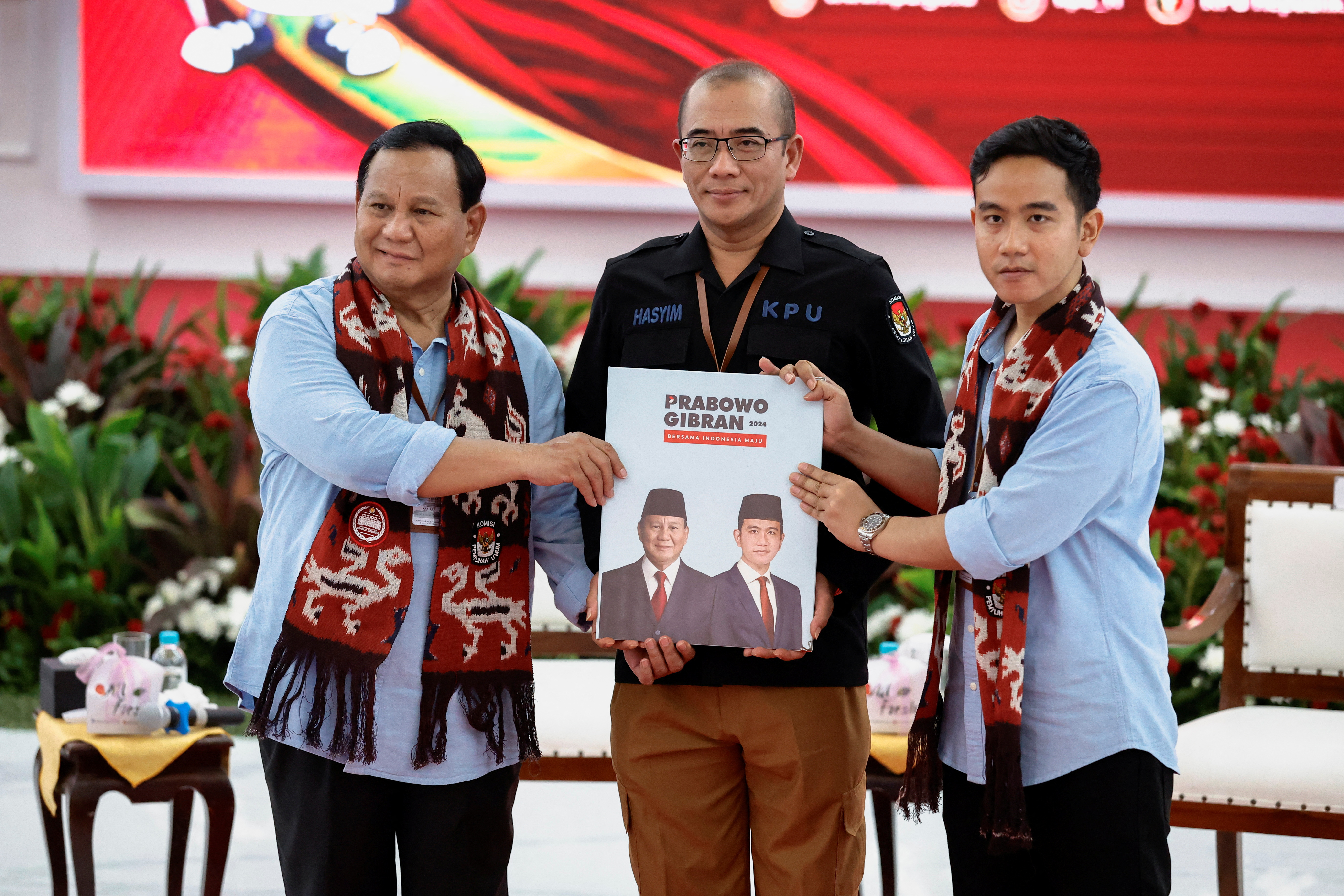 Prabowo and Gibran register their candidacy. They are dressed identically and pasing their registration documents to the head of Indonesia's election commission