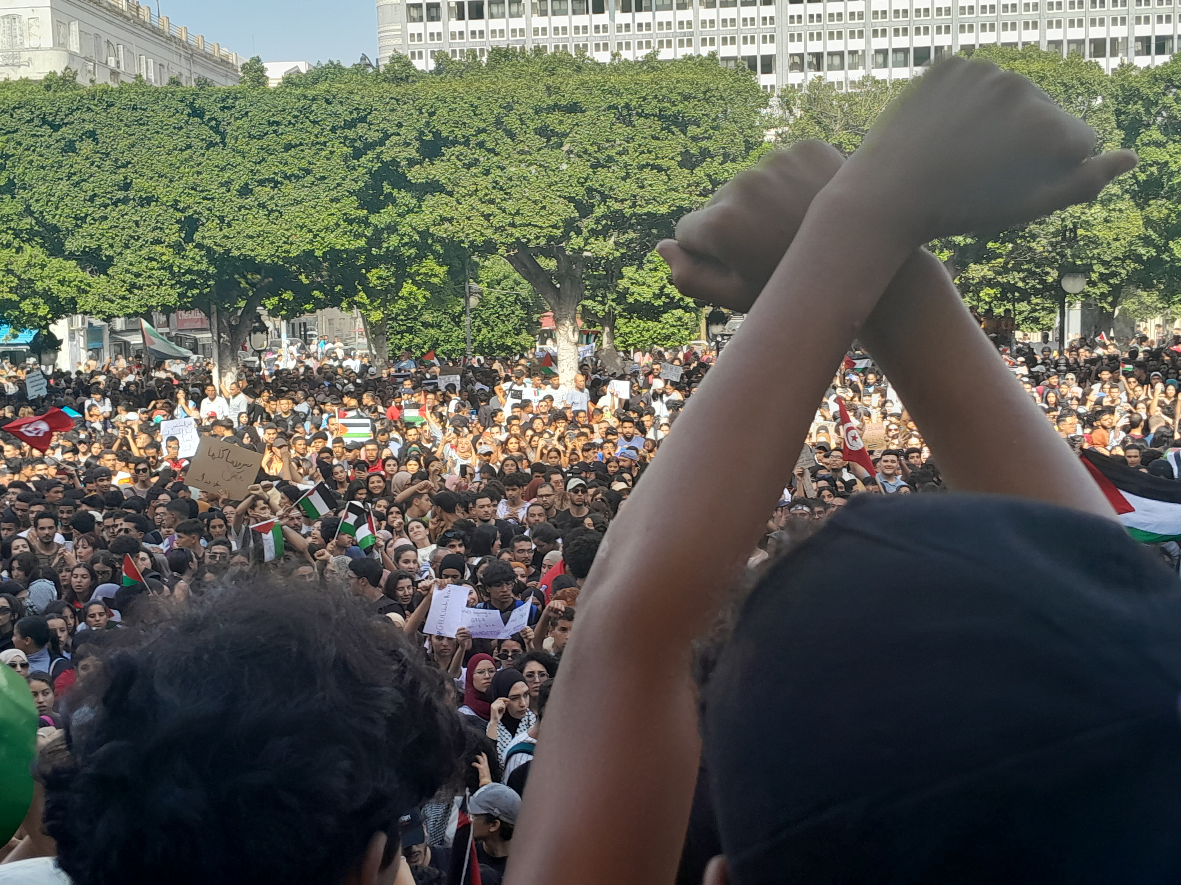 Protesters in Tunis, Tunisia, gather in front of the French embassy. In the foreground, a young protester crosses his arms above his head.