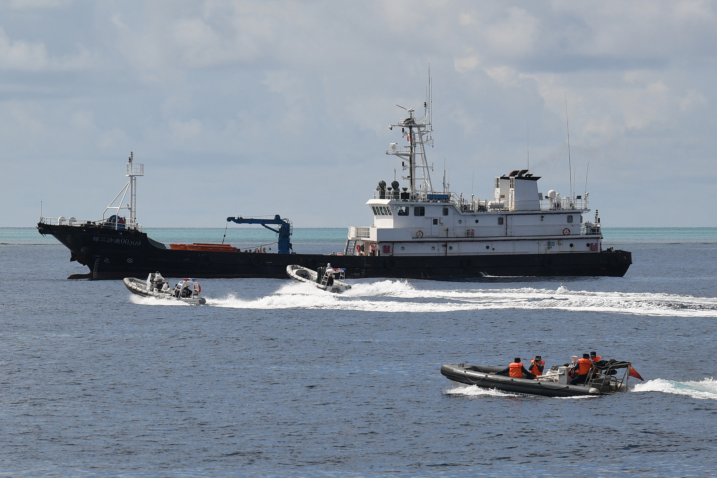 Chinese coastguard personnel on board rigid hull inflatable boats sailing near a Chinese maritime militia vessel.