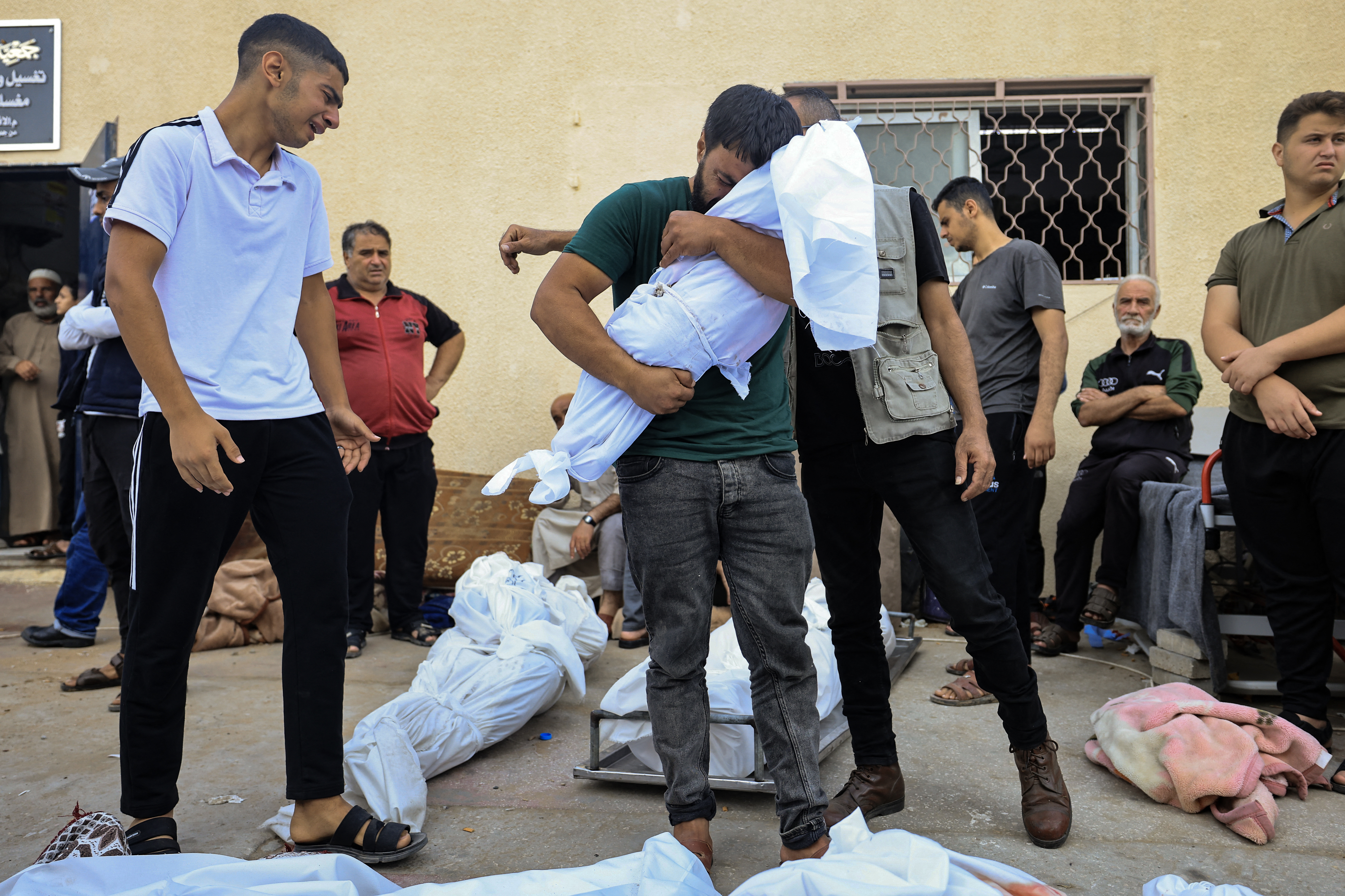 A man reacts as he carries the shrouded body of his child, in front of the morgue of the Al-Aqsa hospital in Deir Balah in the central Gaza Strip, following an Israeli strike on October 22, 2023, as battles continue between Israel and the Palestinian Hamas group. (Photo by Mahmud HAMS / AFP) (AFP)