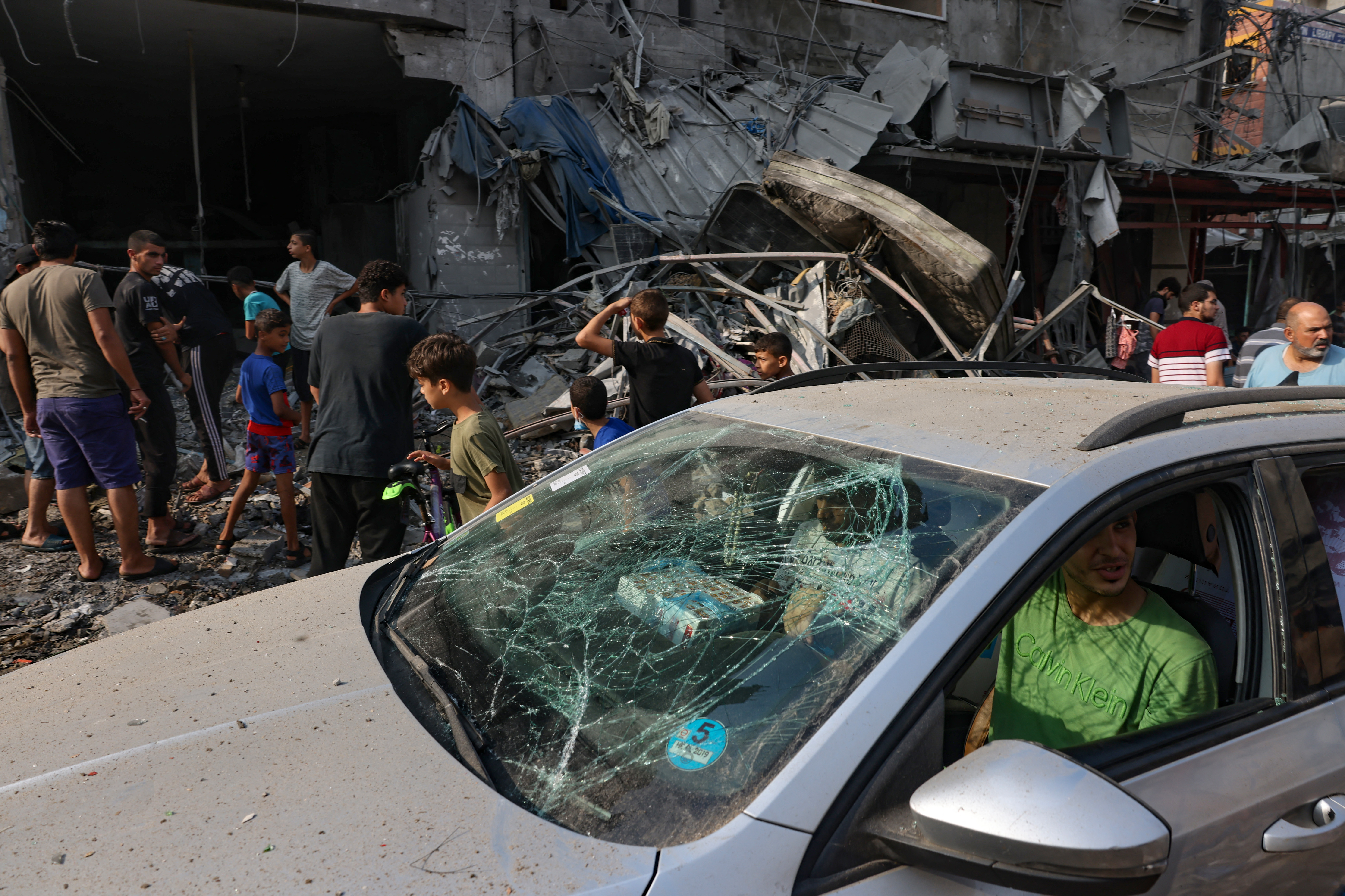 Graphic content / A man drives a damaged car in front of a building destroyed in Israeli strikes on Al-Shatee camp in Gaza City