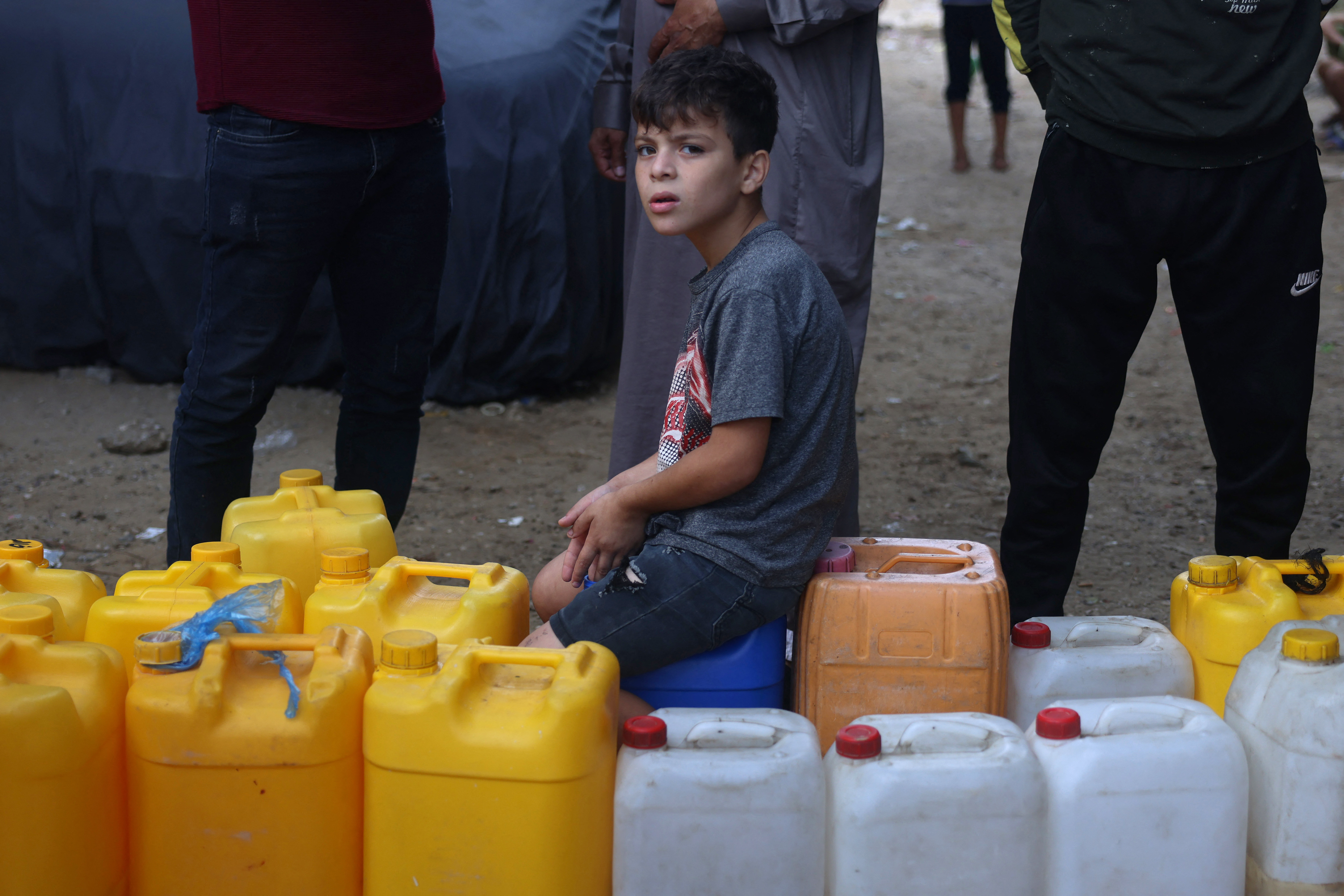 A young Palestinian sit on plastic jerrycans at a water filling point, in Rafah in the southern Gaza Strip