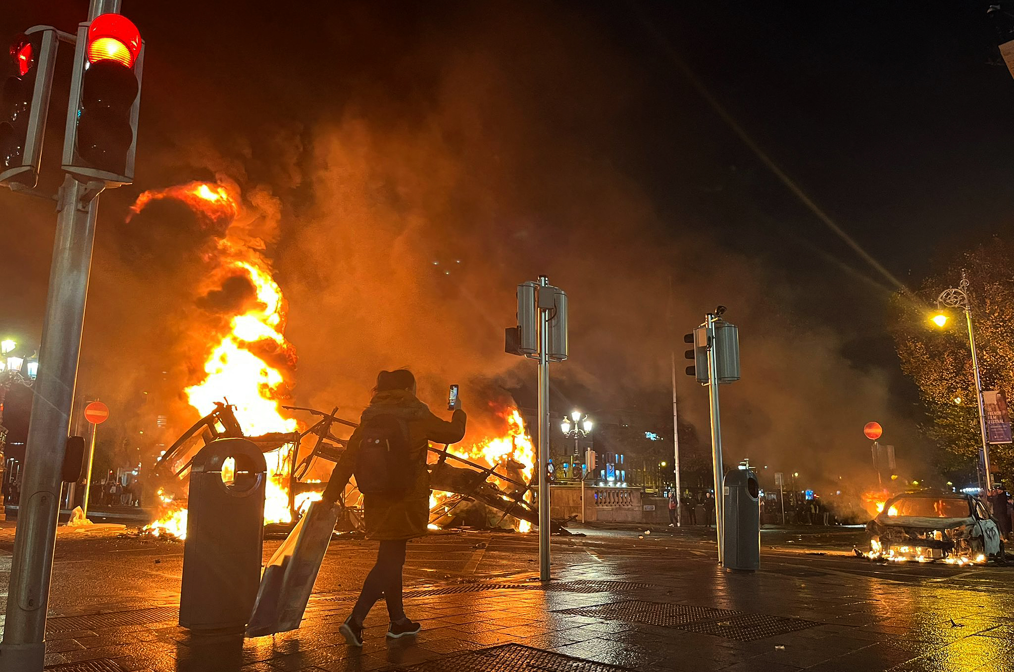 Flames rise from the car and a bus,