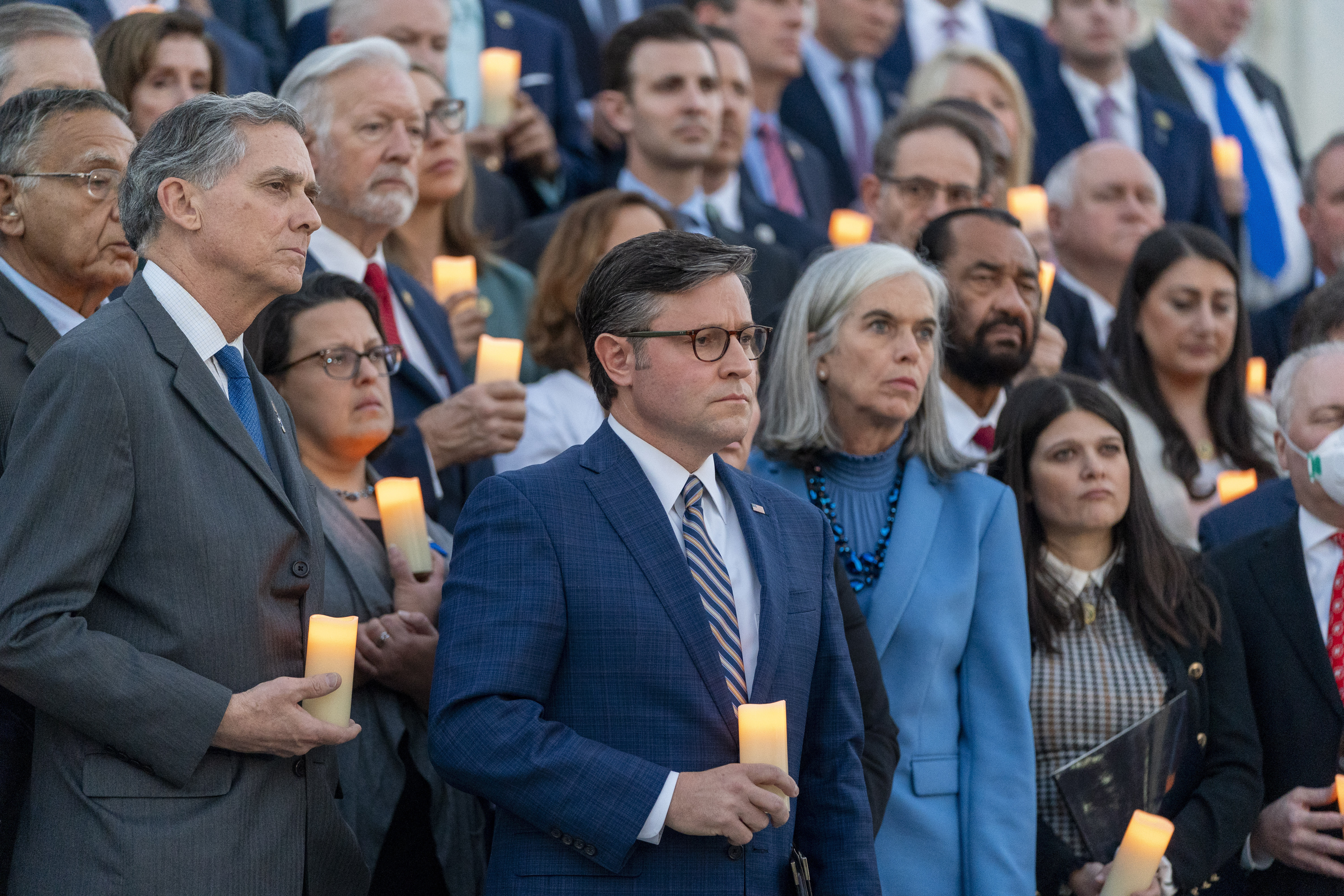Mike Johnson and other members of Congress stand on the steps of Congress, each holding a small votive candle.