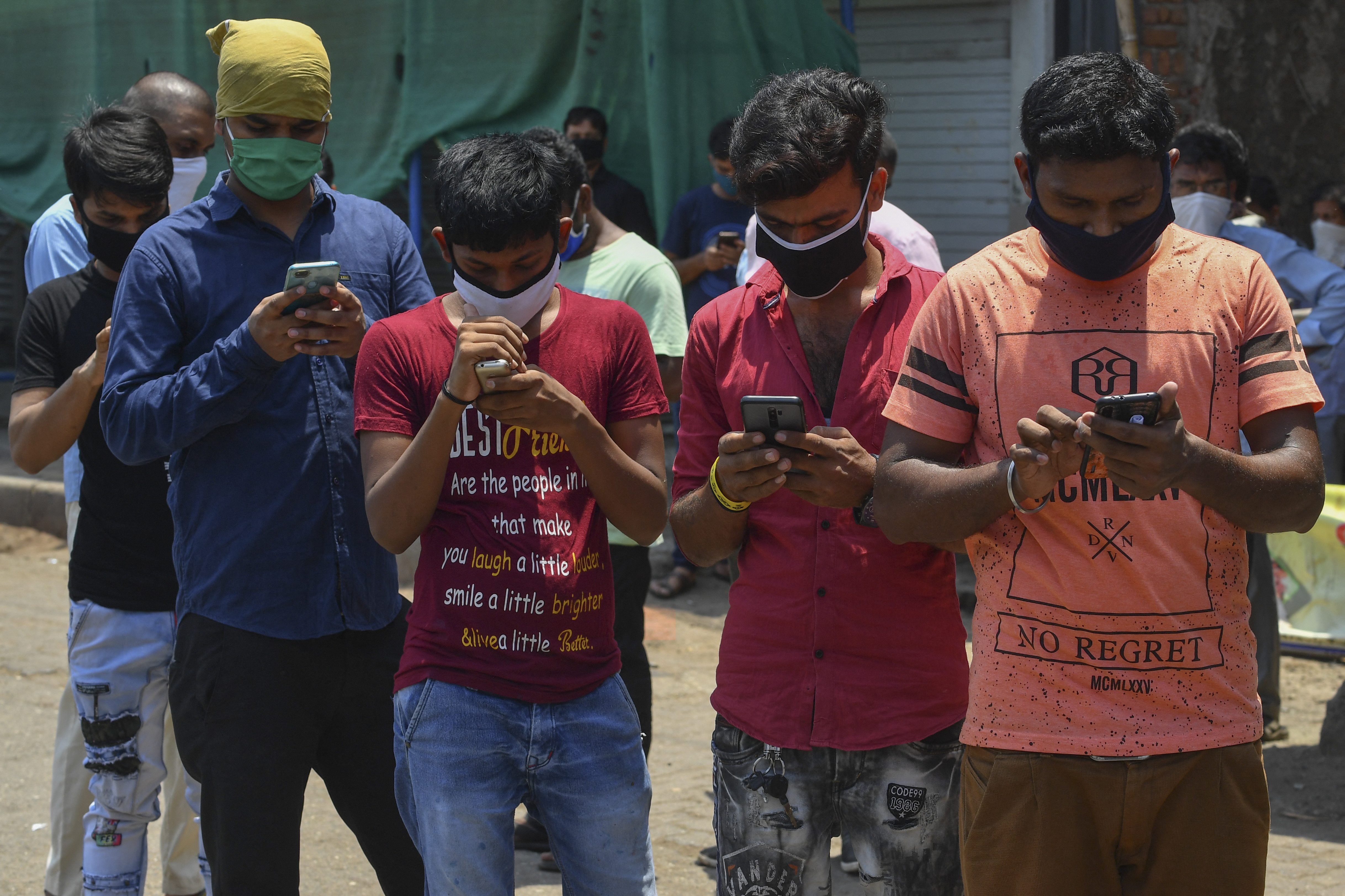 Stranded migrant workers look at their mobile phones as they register for special transportations organized to bring them back to their hometowns during a government-imposed nationwide lockdown as a preventive measure against the spread of the COVID-19 coronavirus, in Mumbai, India