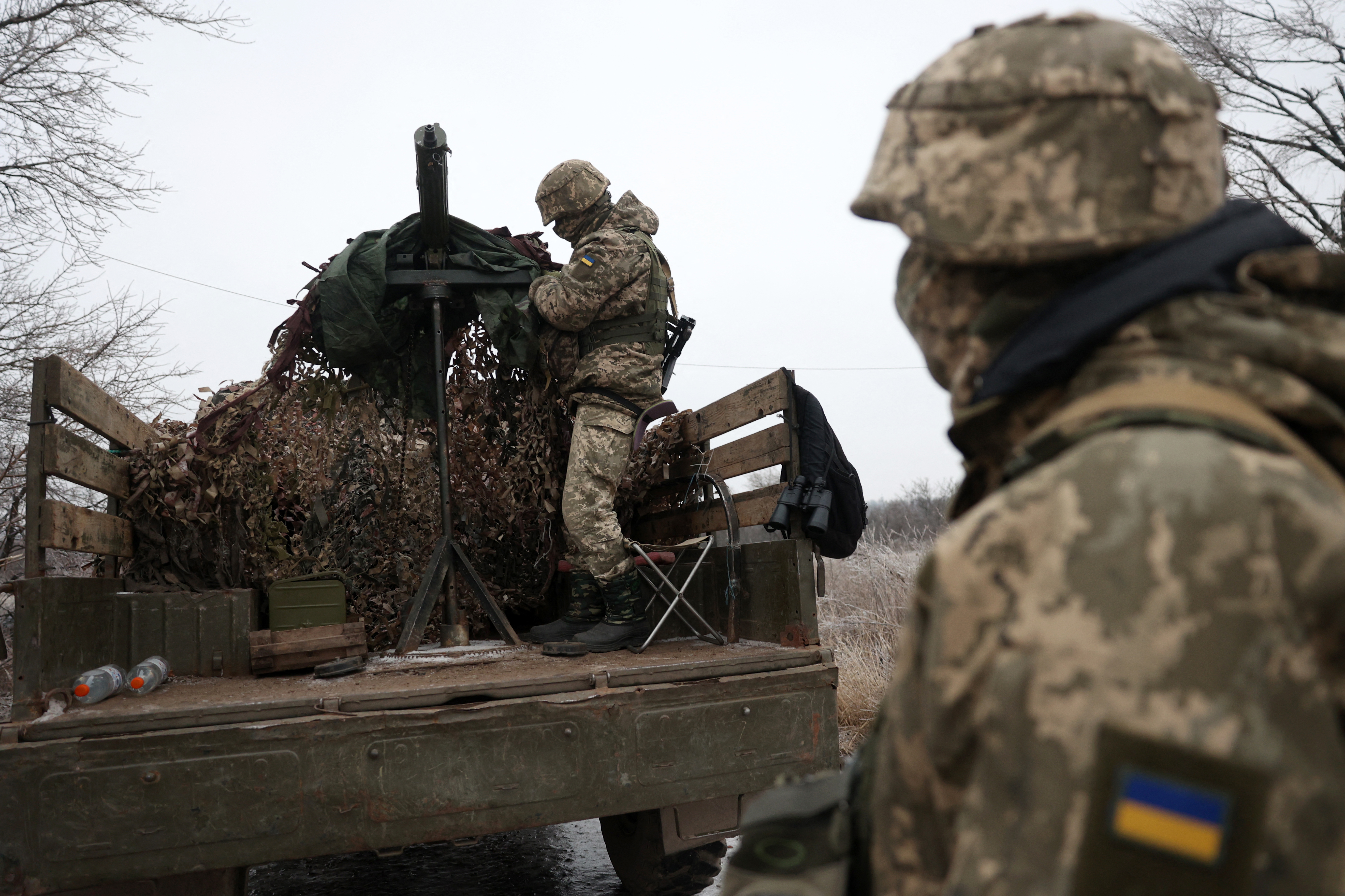 Two Ukrainian soldiers on the front line in Donetsk. One is on the back of a truck that is carrying a weapon