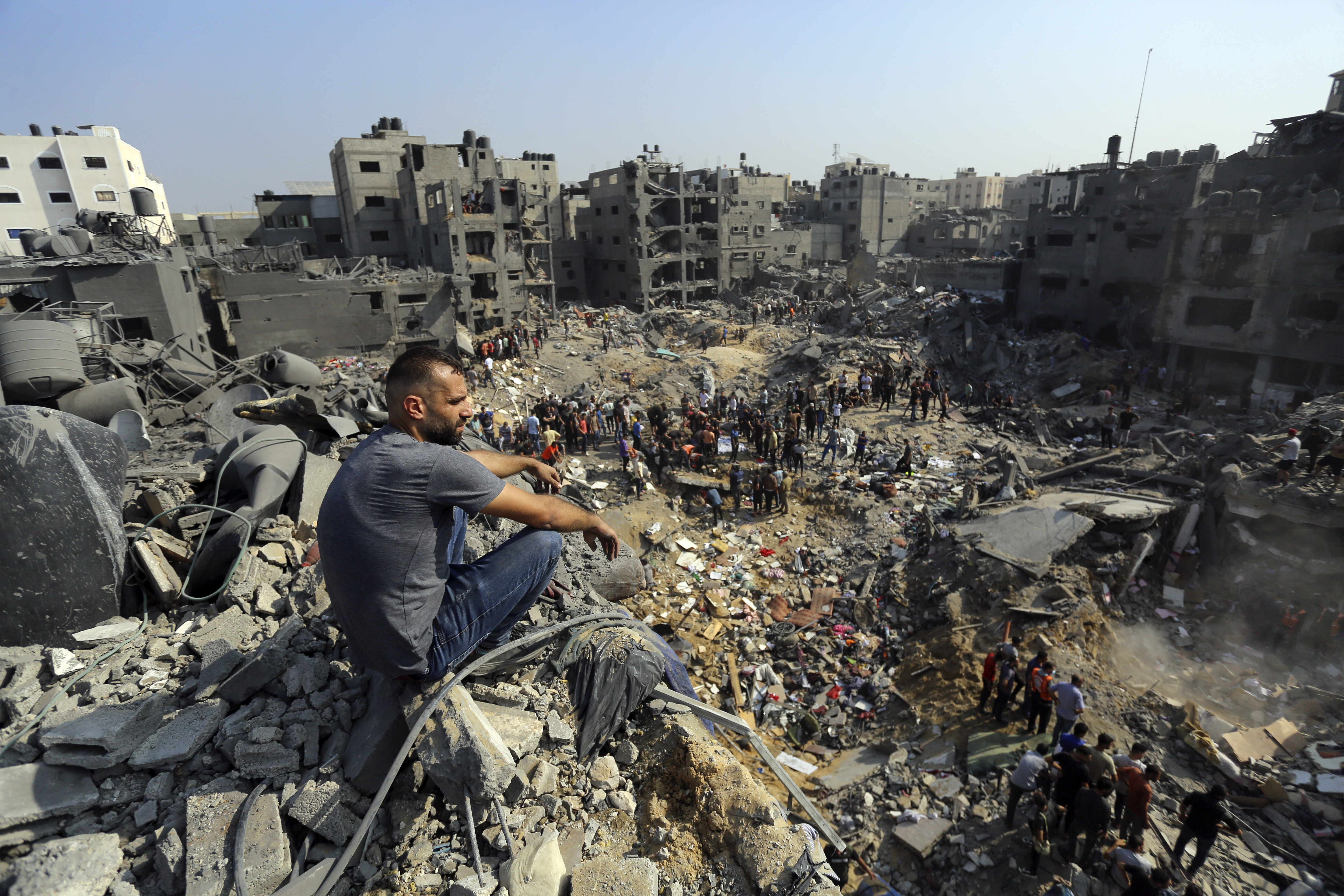 A man sits on the rubble as others wander among debris of buildings that were targeted by Israeli airstrikes in Jabaliya refugee camp, northern Gaza Strip