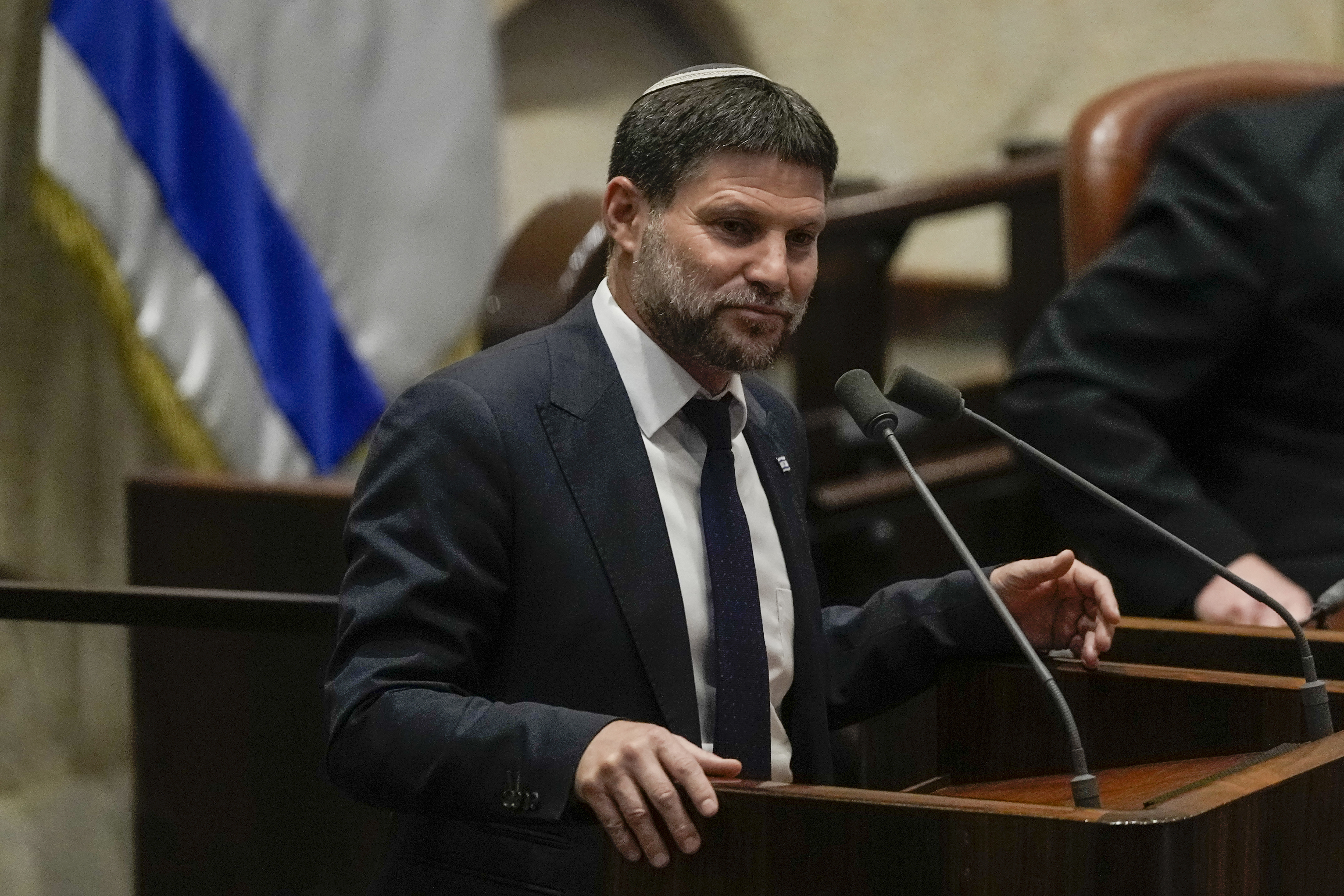 a man in a suit speaks in front of an Israeli flag