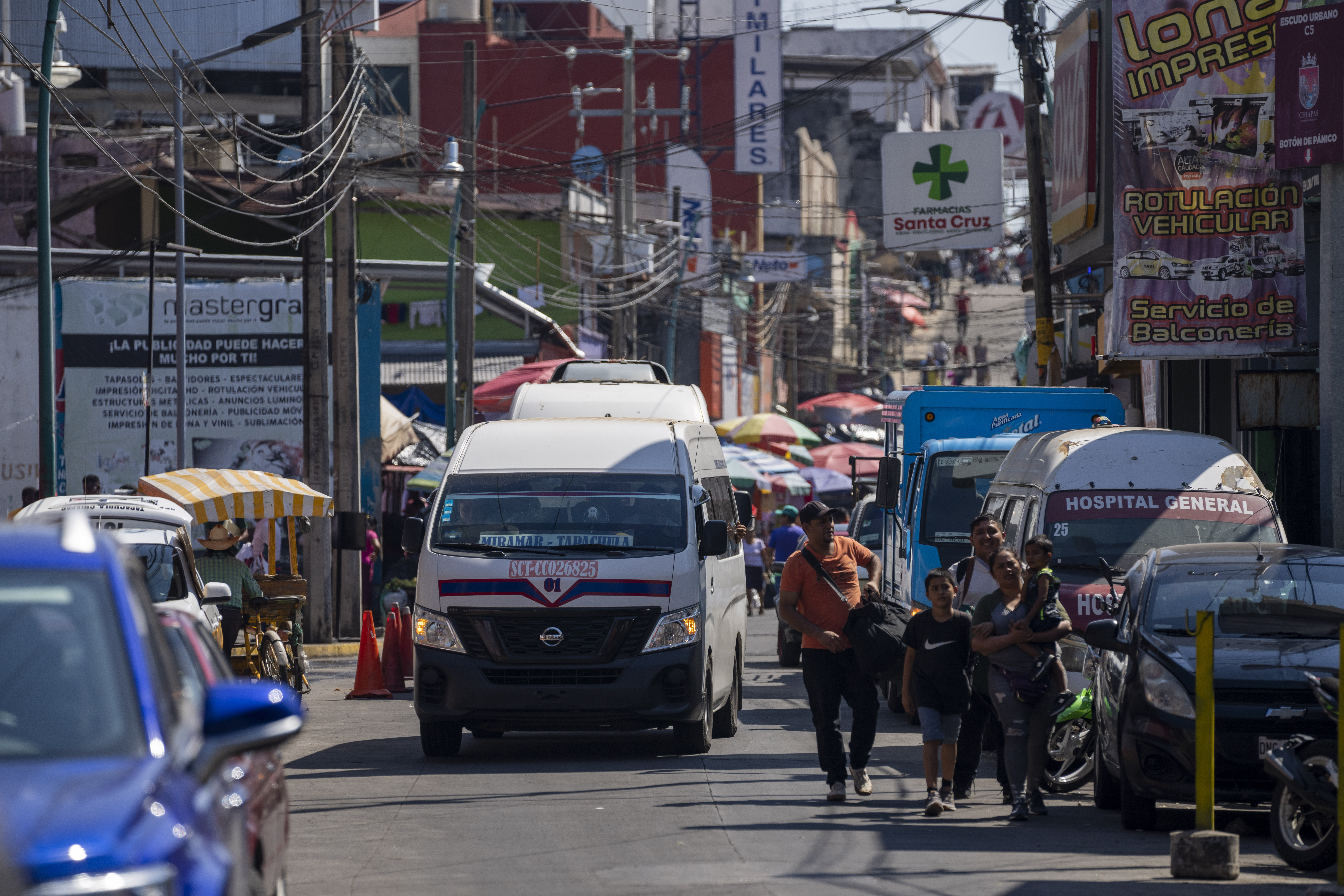 A bus travels along a busy street in Tapachula, Mexico. A family walks along the roadside.