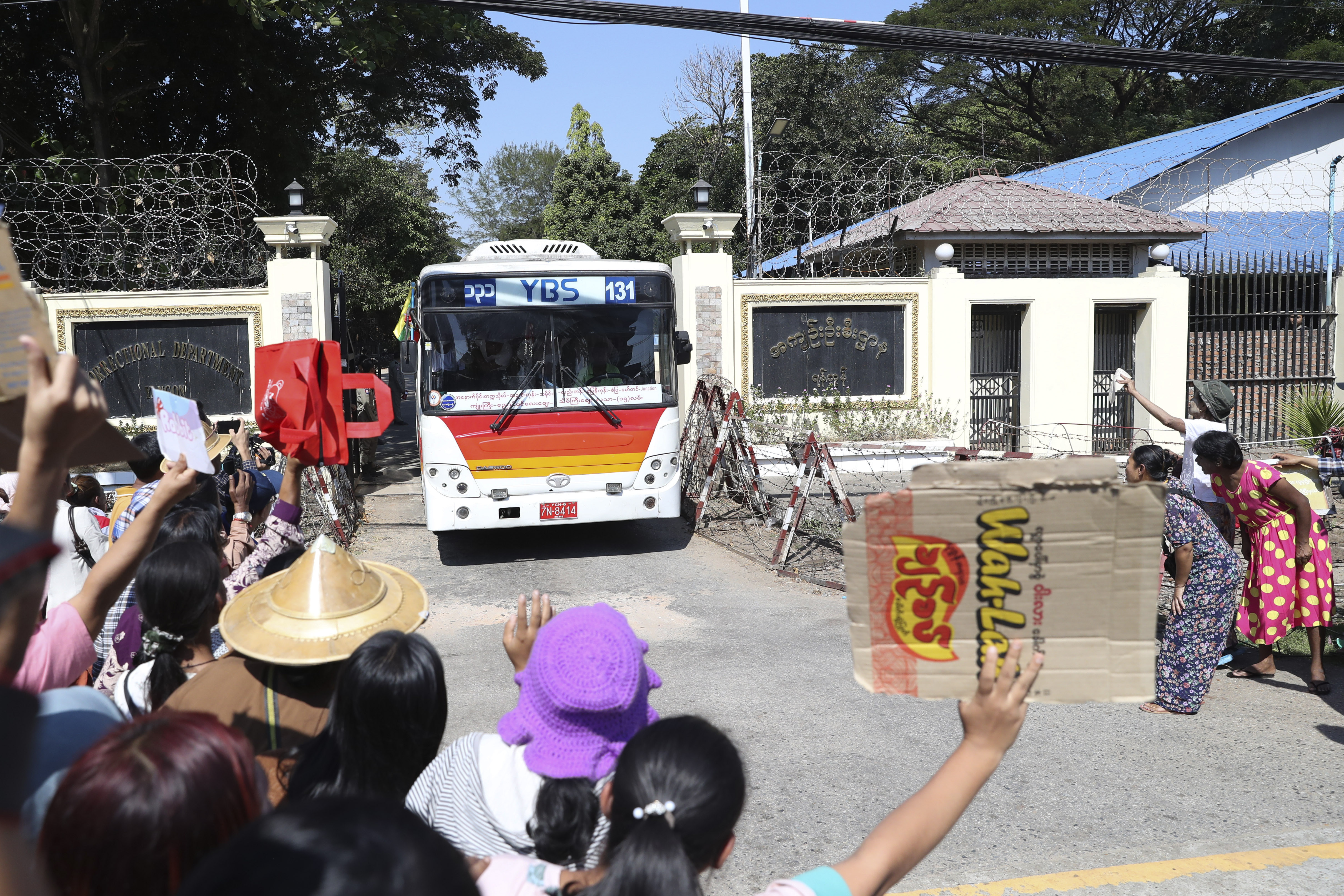 A bus leaving Insein prison with those released. There are family members waiting outside the gate, which is topped with razor wire