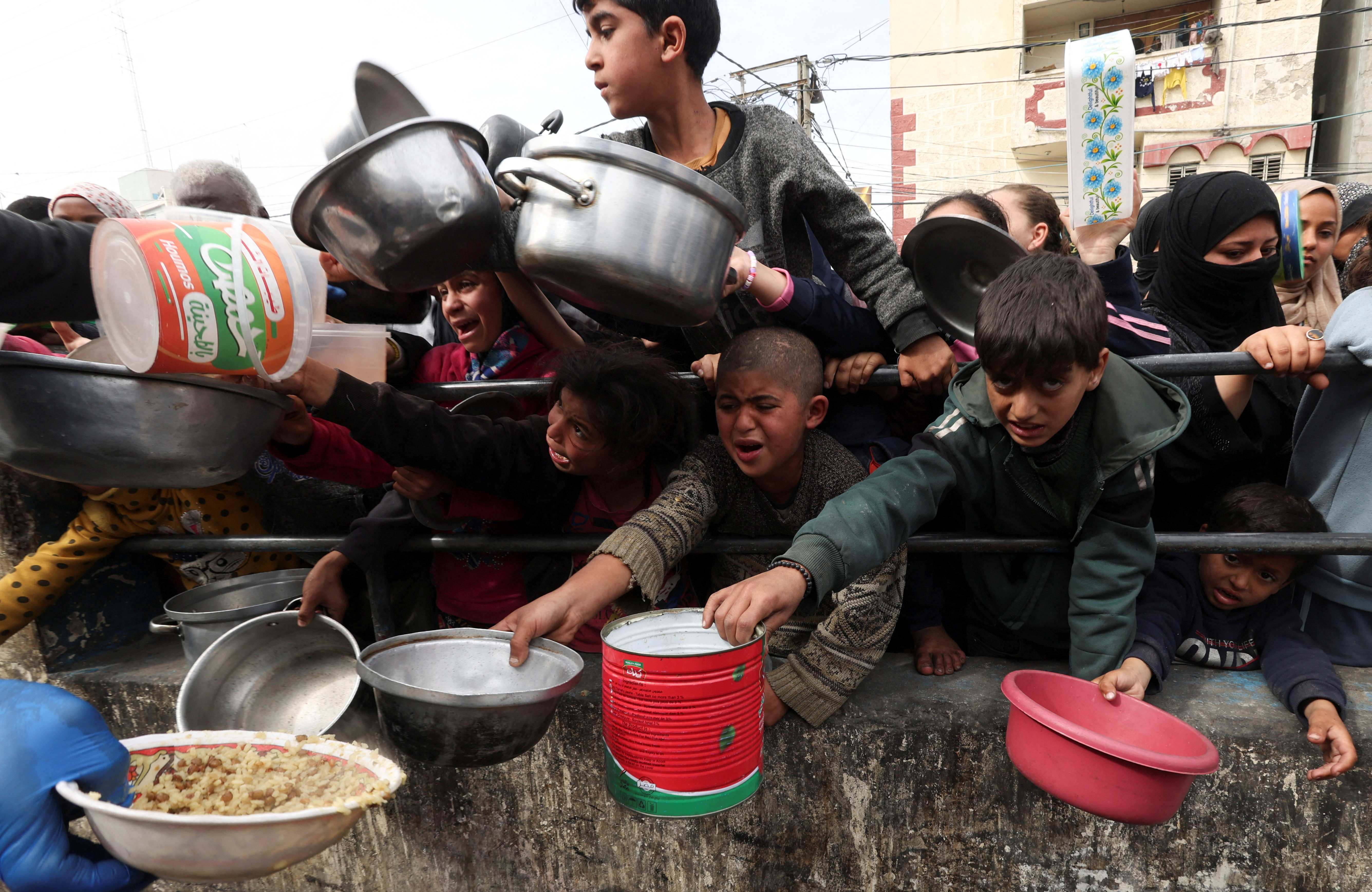 Palestinian children wait to receive food cooked by a charity kitchen amid shortages of food supplies, in the southern Gaza Strip, February 13, 2024 [Ibraheem Abu Mustafa/Reuters]