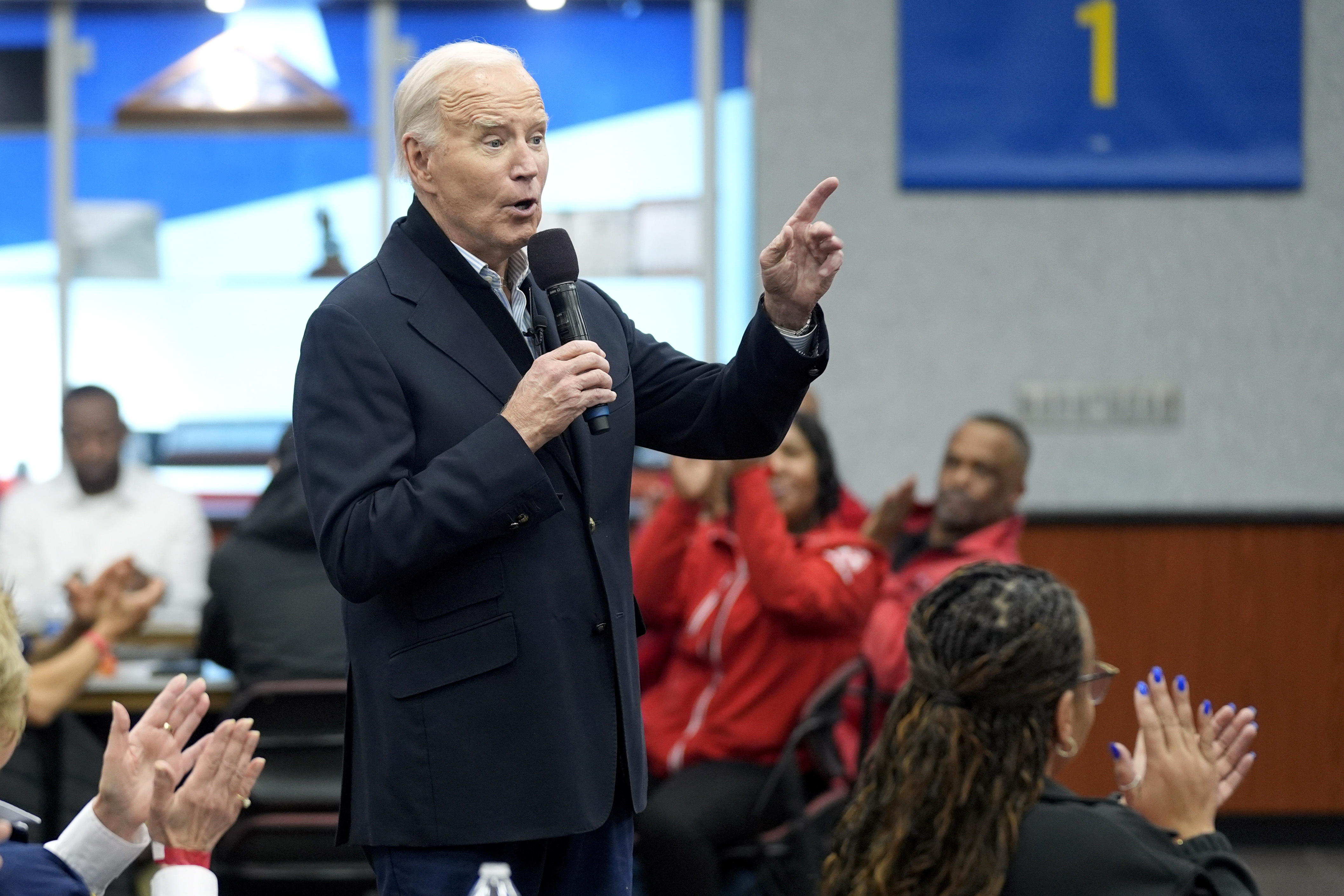 Joe Biden speaks into a handheld microphone and lifts a finger in gesture at a campaign stop.