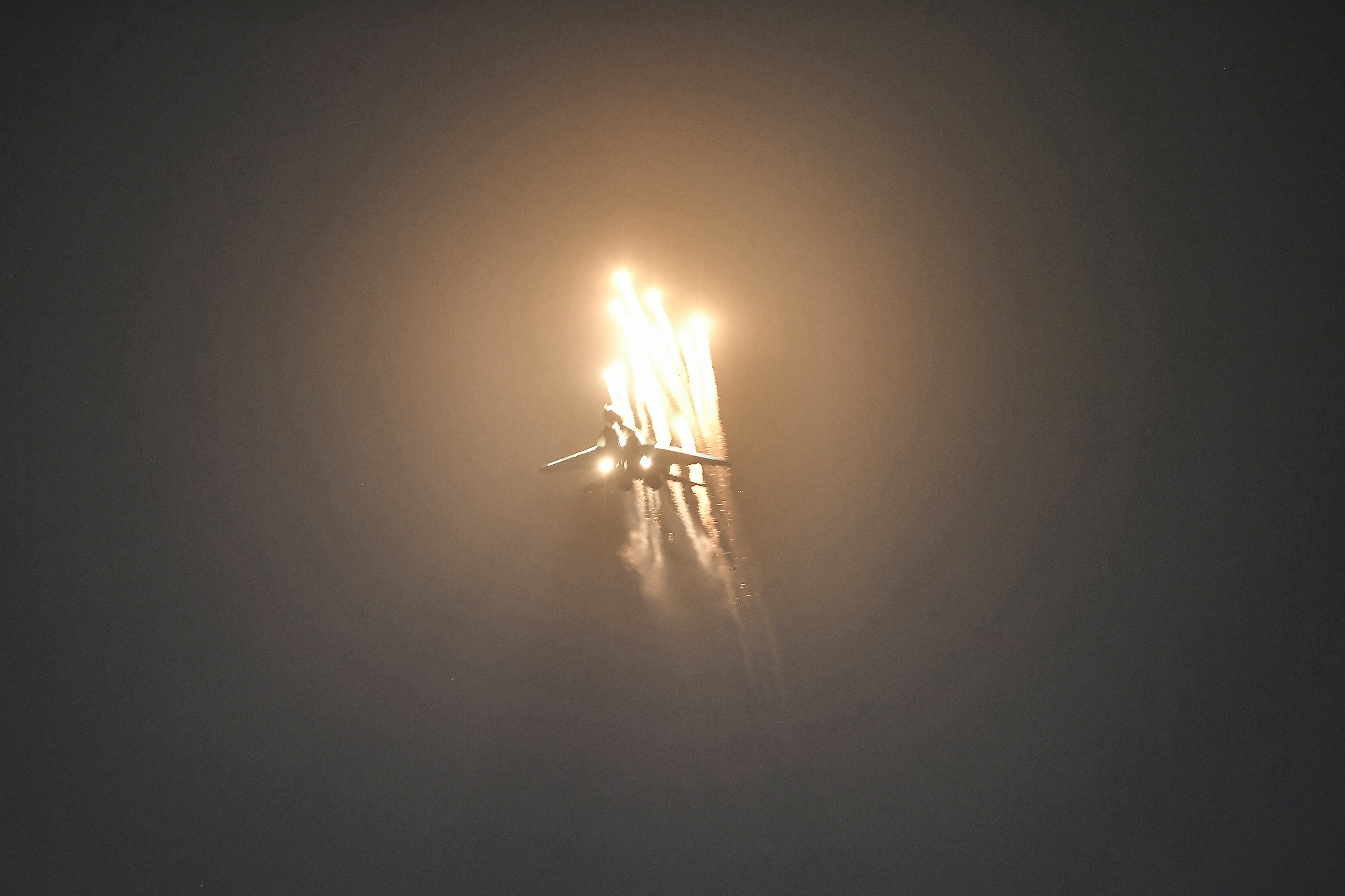 A Sukhoi Su-30 fighter takes part in an aerial display it is releasing flares with the flames lighting up the night sky.
