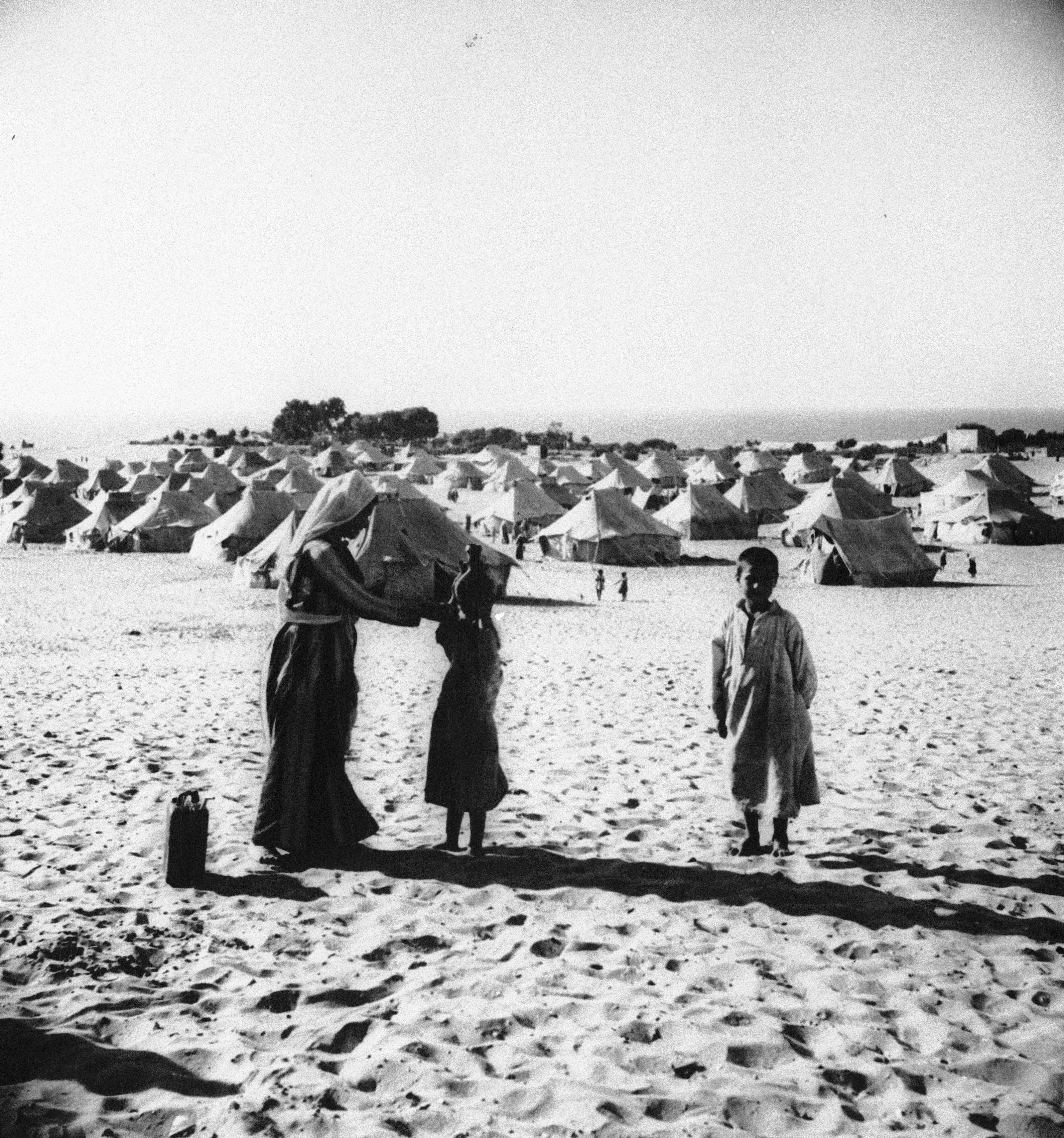 A mother and her children are seen at tent city in the Gaza area of Egyptian-occupied Palestine where about 216,000 Arab refugees live in worn-out tents, July 23, 1949. The woman is teaching her daughter how to carry a water jug on her head. (AP Photo/S. Swinton)