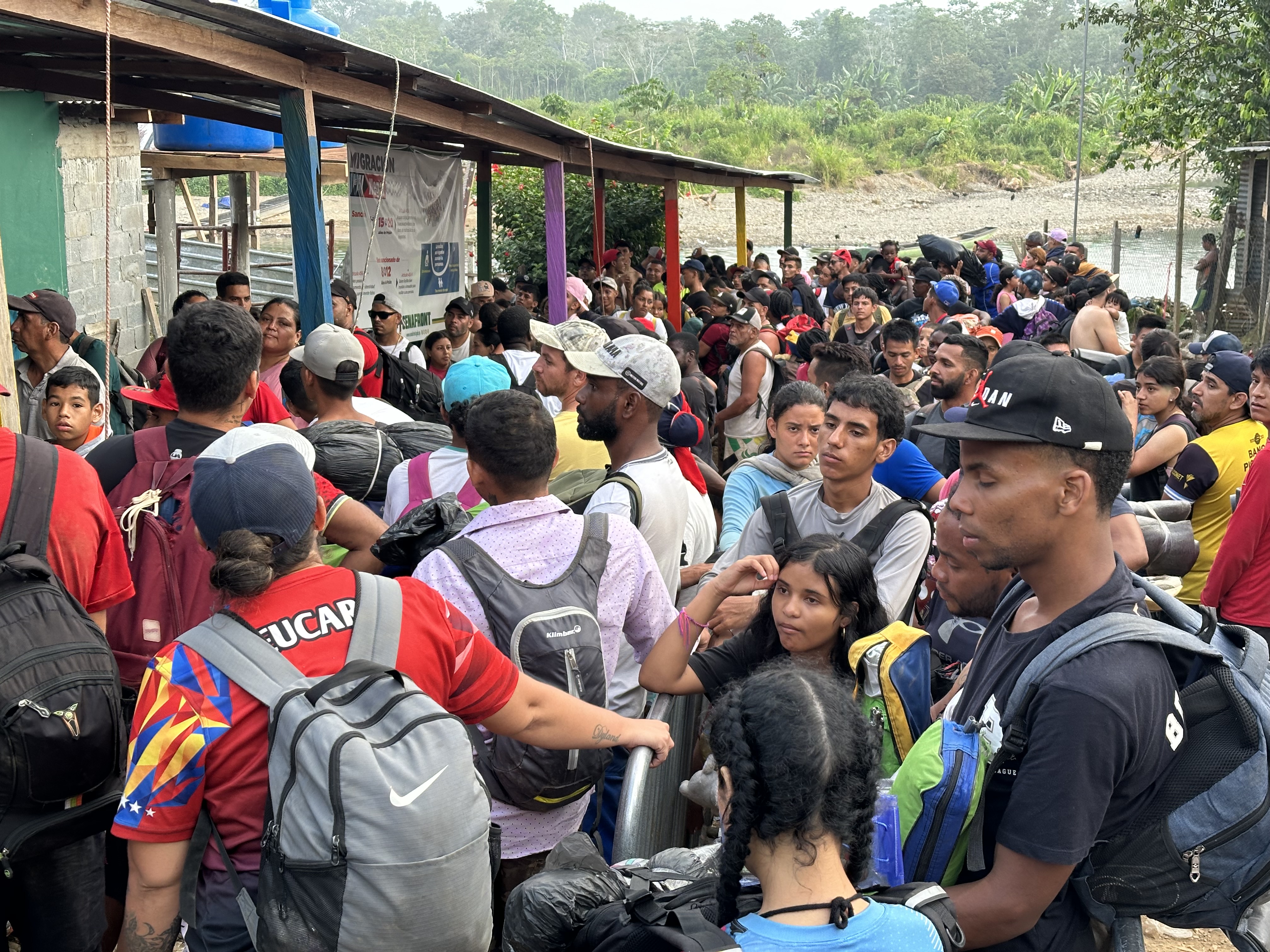A crowd of migrants and asylum seekers approach a low-slung building in Bajo Chiquito.