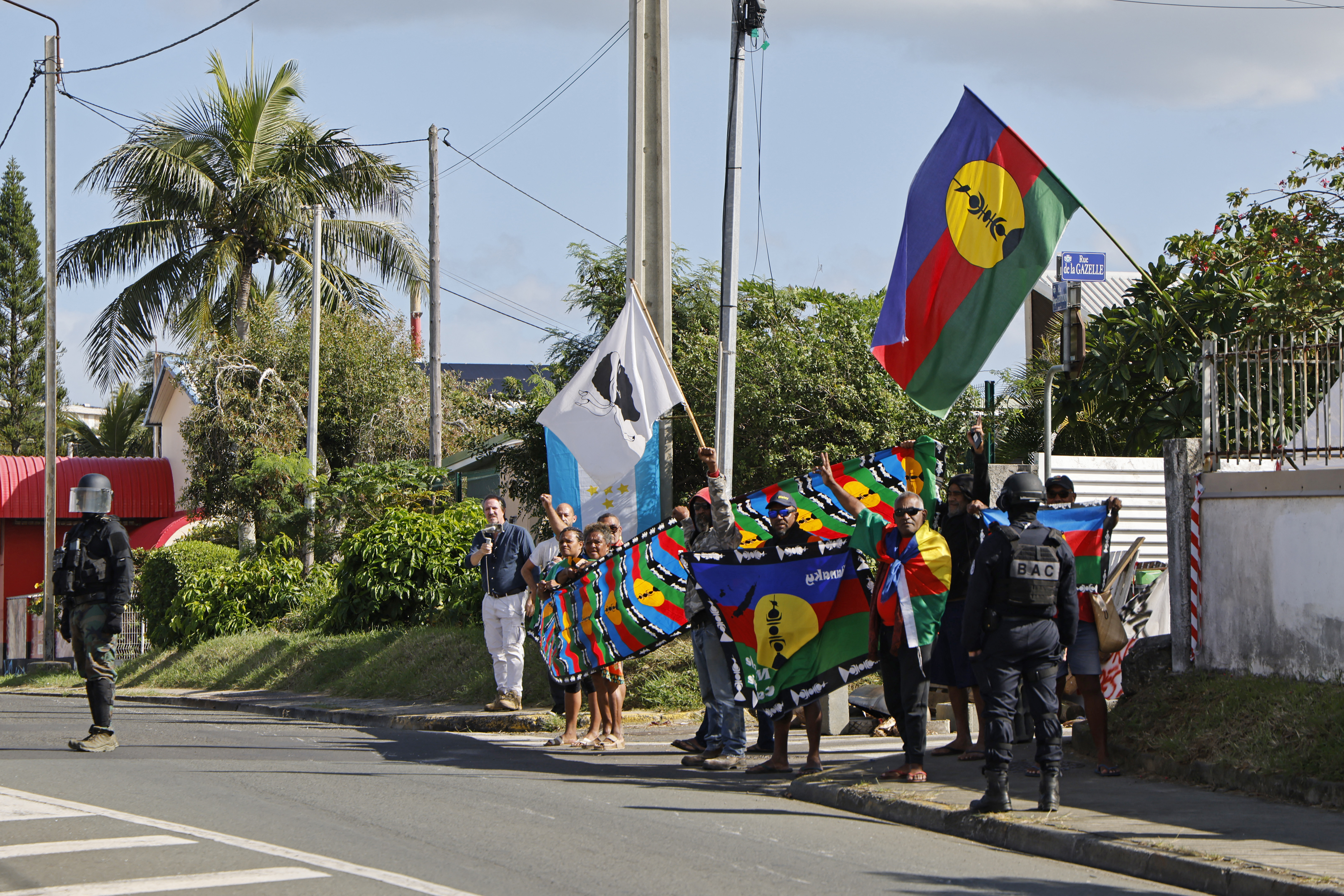 people hold brightly coloured flags on a tropical street