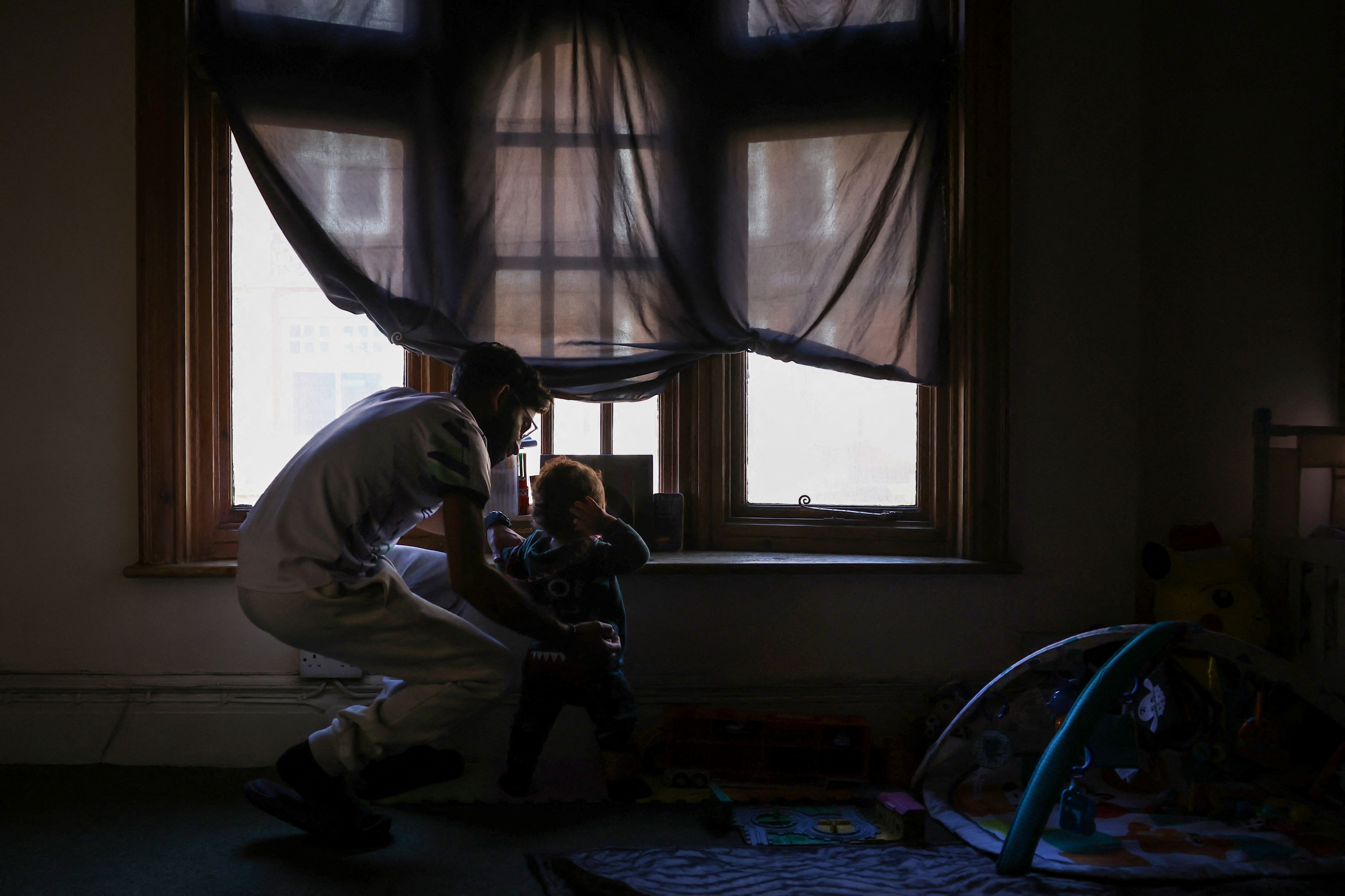 A man closes the curtain as his son looks out the window of their home, in what was once a solicitors office, an empty building which squatter activist group Reclaim Croydon occupied, in Croydon, south London, Britain, February 12