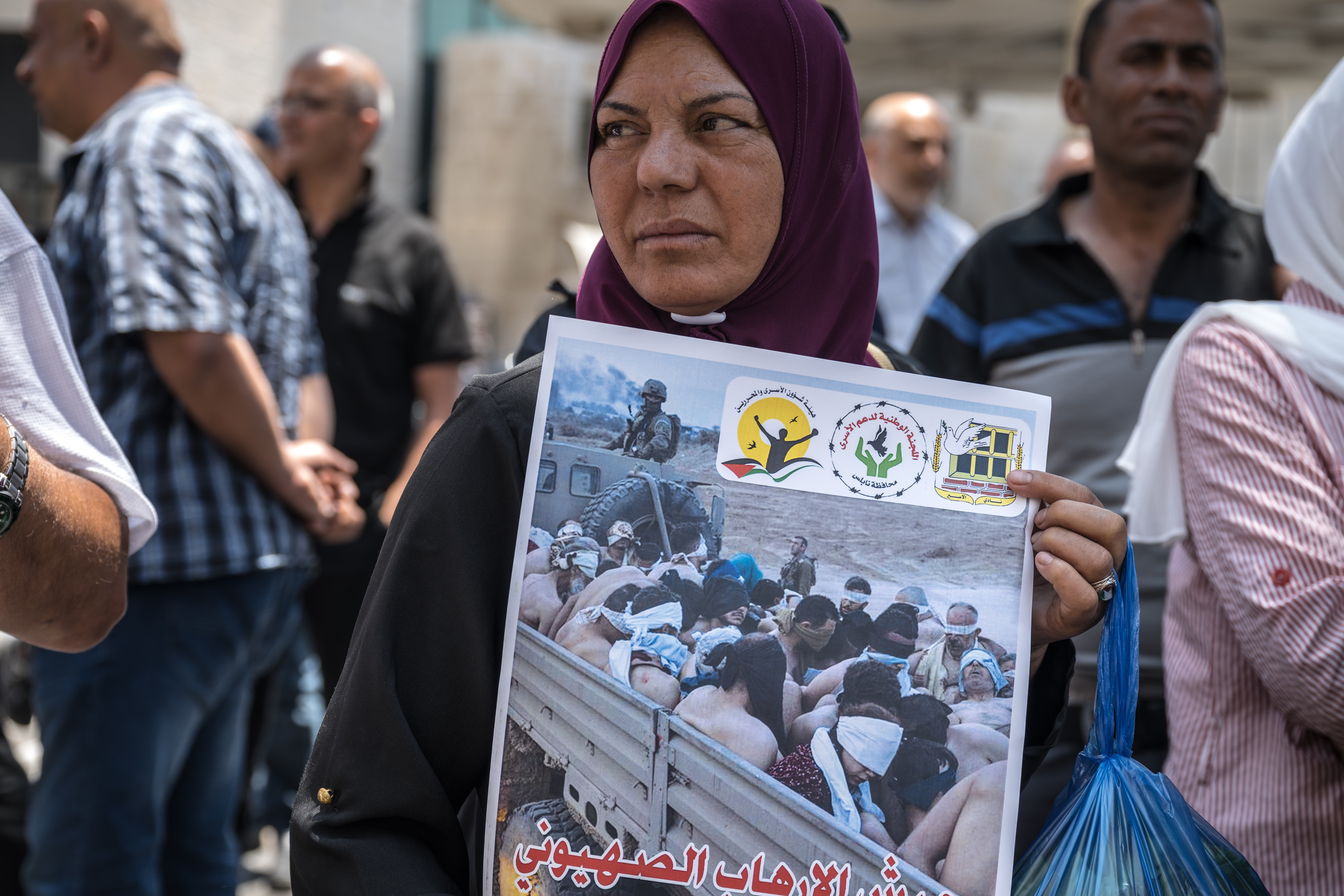 a woman holds a poster showing detained prisoners at a protest