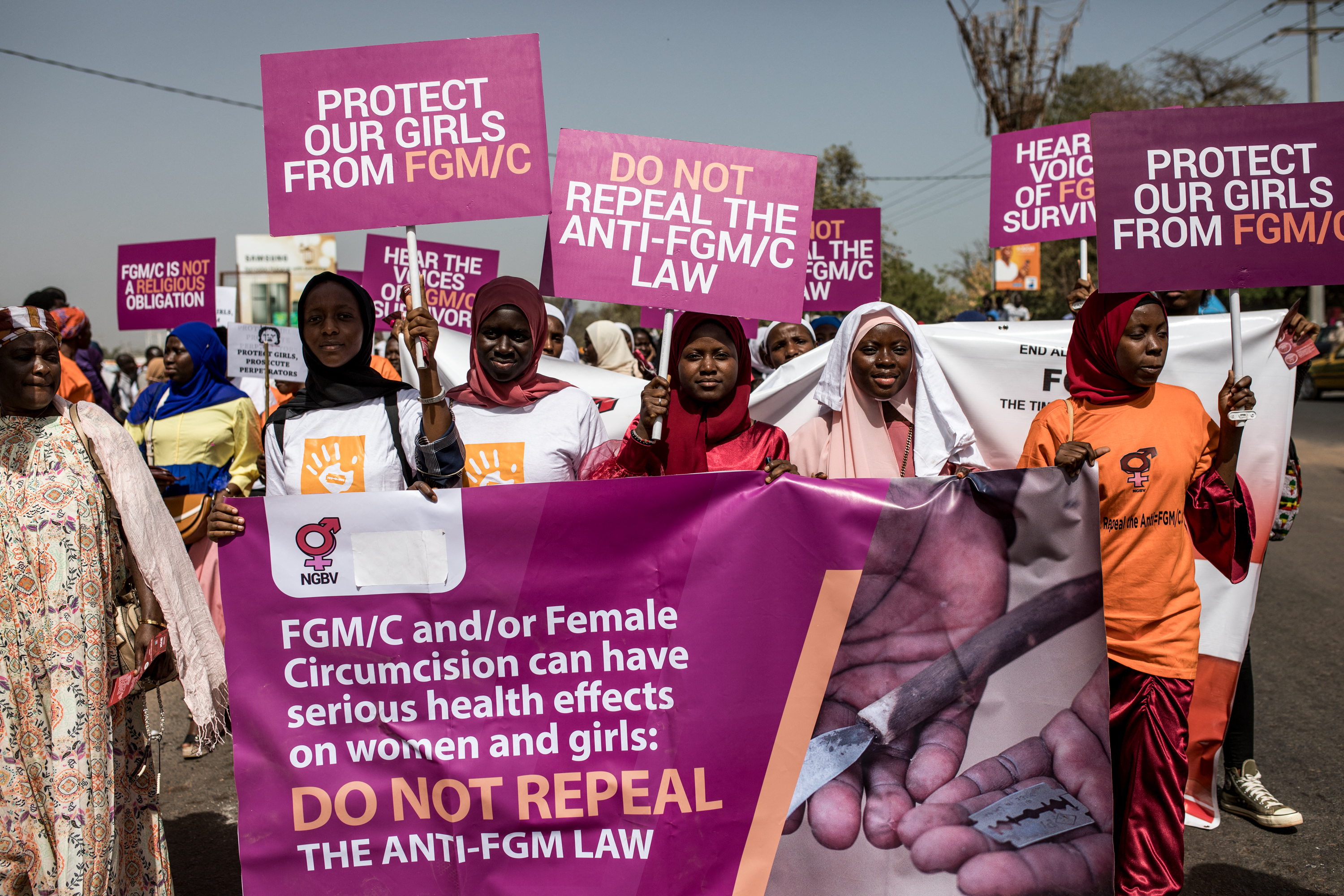 Anti Female Genital Mutilation (FGM) protesters hold placards outside the National Assembly in Banjul on march 18, 2024, during the debate between lawmakers on a highly controversial bill seeking to lift the ban on FGM. Gambian lawmakers voted on March 18, 2024 to advance to the next parliamentary stage a highly controversial bill that seeks to lift a ban on female genital mutilation (FGM), which has been in place since 2015. The issue has divided the tiny West African nation for months, with hundreds gathering to protest outside parliament. (Photo by MUHAMADOU BITTAYE / AFP)