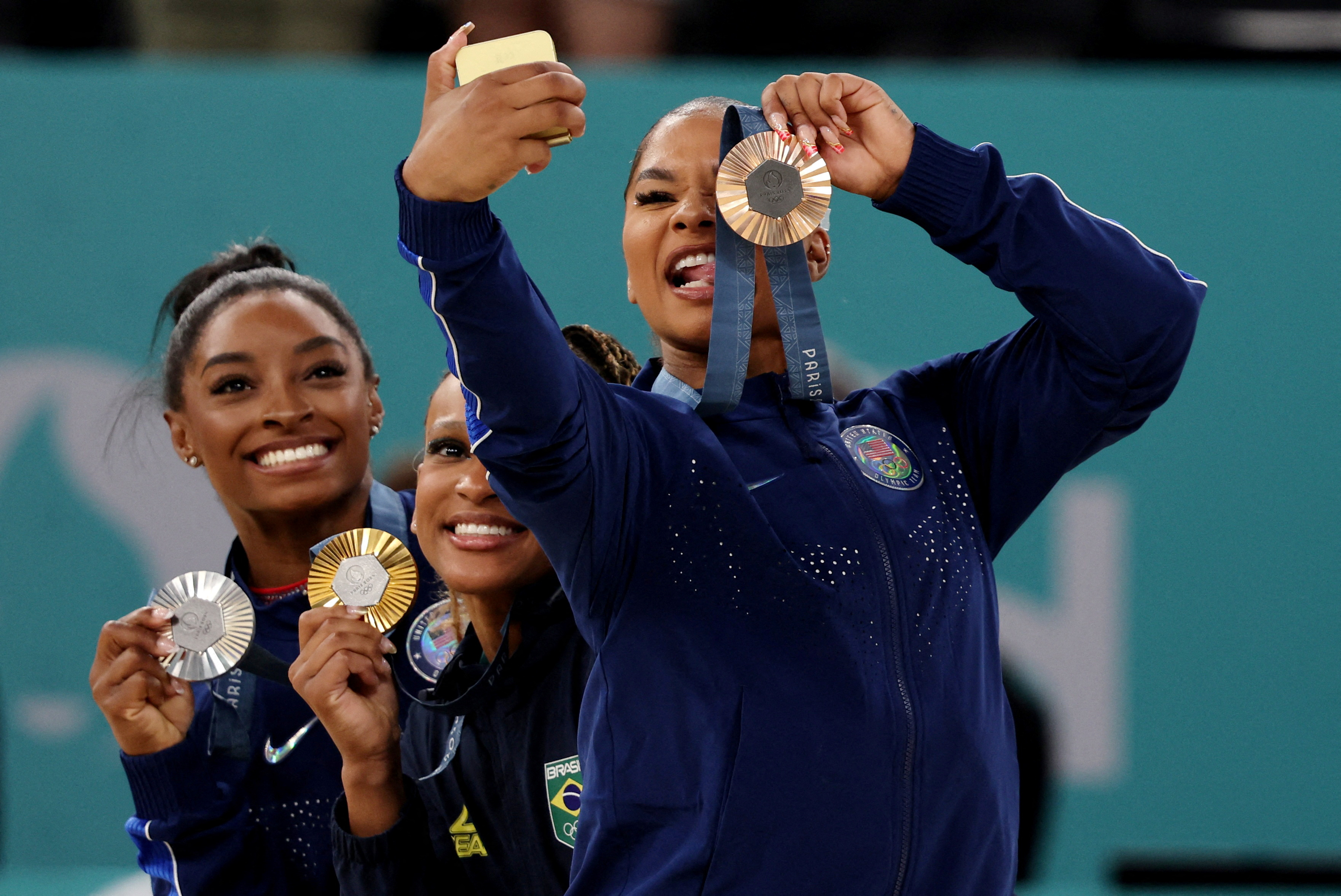 Gold medallist Rebeca Andrade of Brazil celebrates on the podium with silver medallist Simone Biles and bronze medallist Jordan Chiles, both from the United States, on August 05, 2024 [Mike Blake/Reuters]