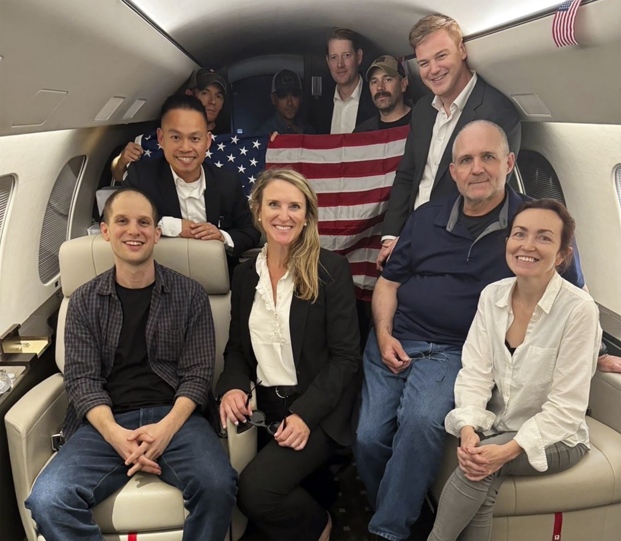 Evan Gershkovich (left) Alsu Kurmasheva (right) and Paul Whelan, (second from right) sitting with others freed from Russian prisons on board a private jet. They look happy and relieved.