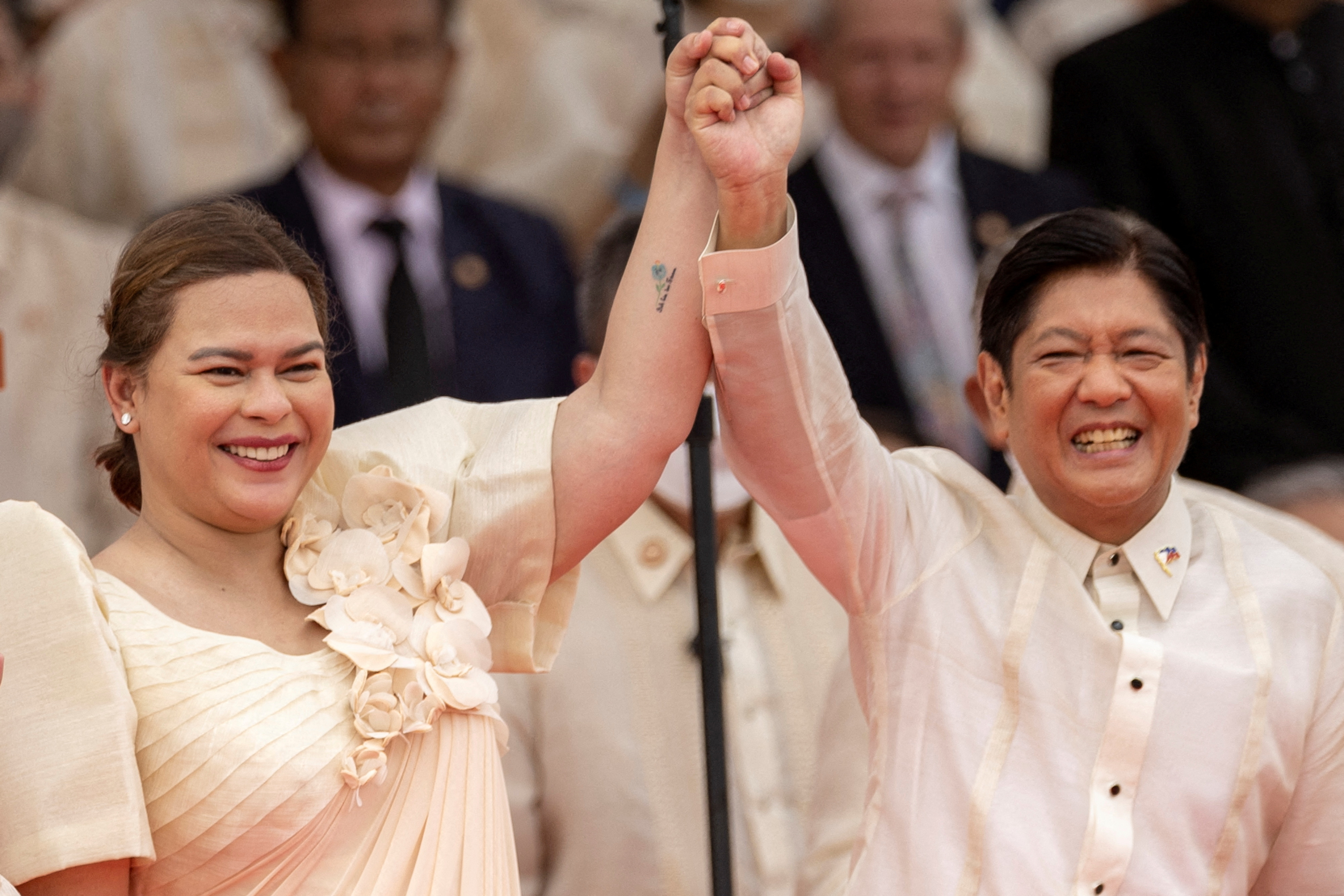 Vice President Sara Duterte and President Ferdinand Marcos Jr raise their linked arms and smile.