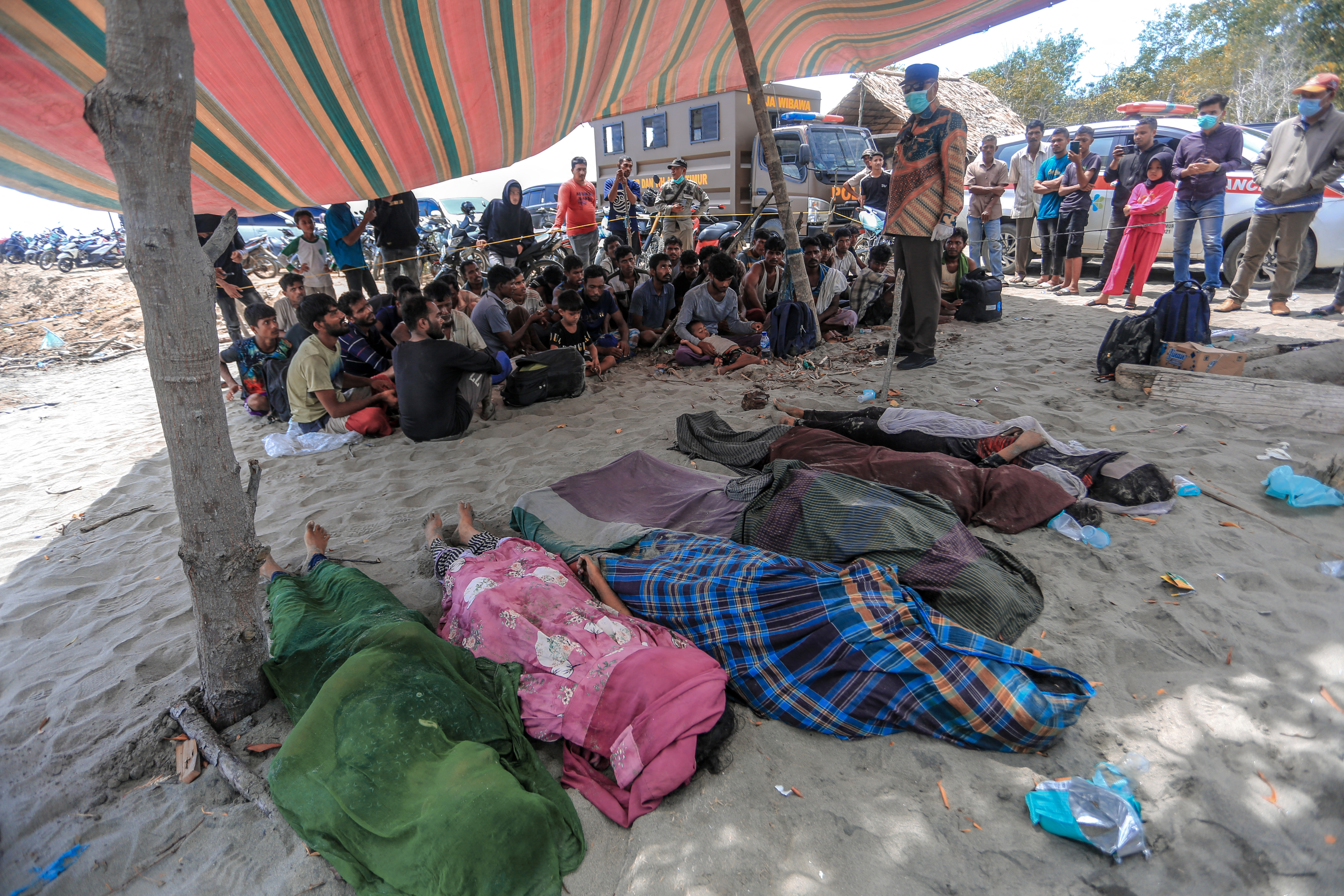 The bodies of Rohingya refugees are seen past surviving members of the persecuted minority, who were left stranded on the coast at Meunasah Asan village