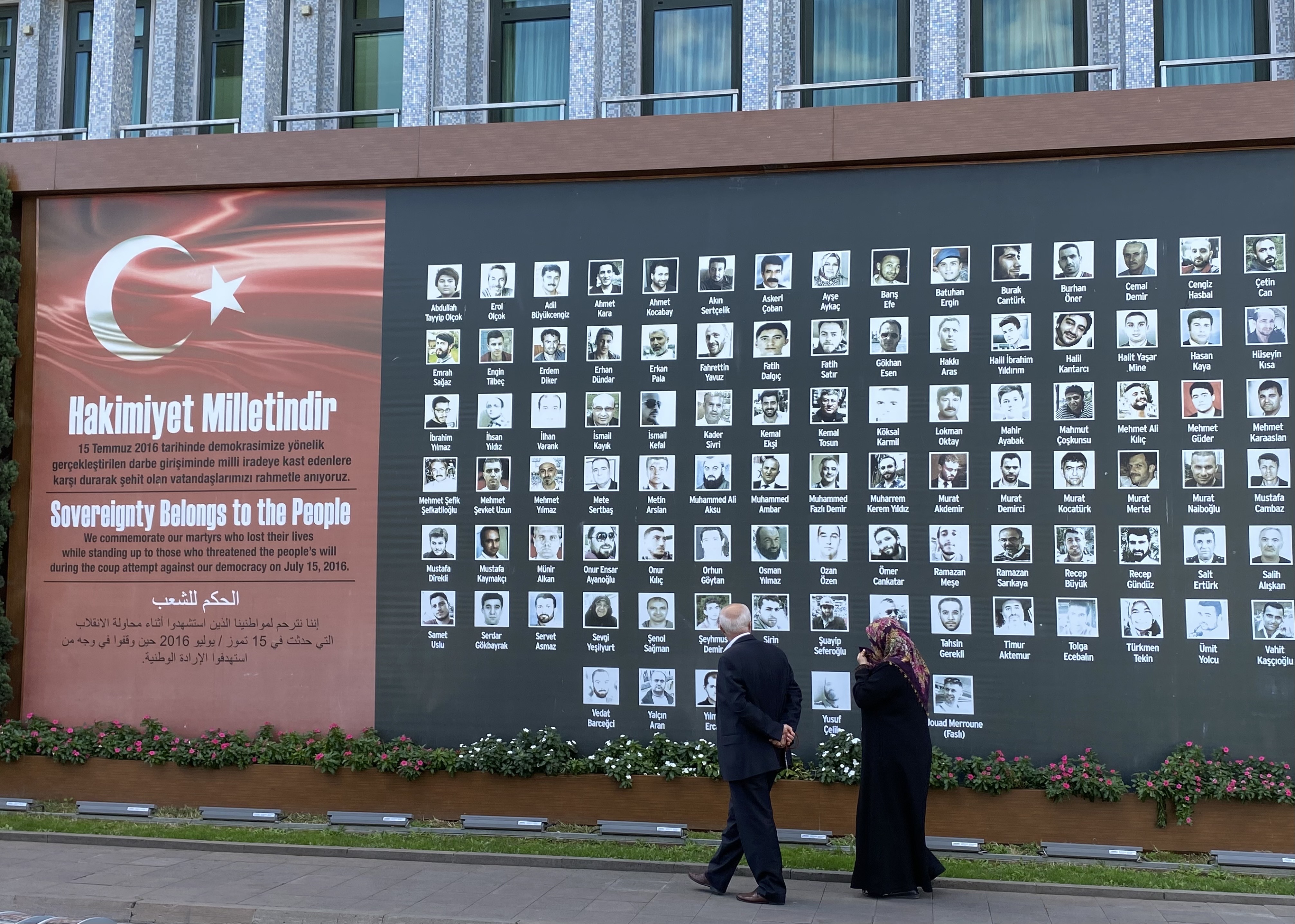 An elderly couple standing in front of a photo memorial of people that were killed during the 2016 coup attempt.