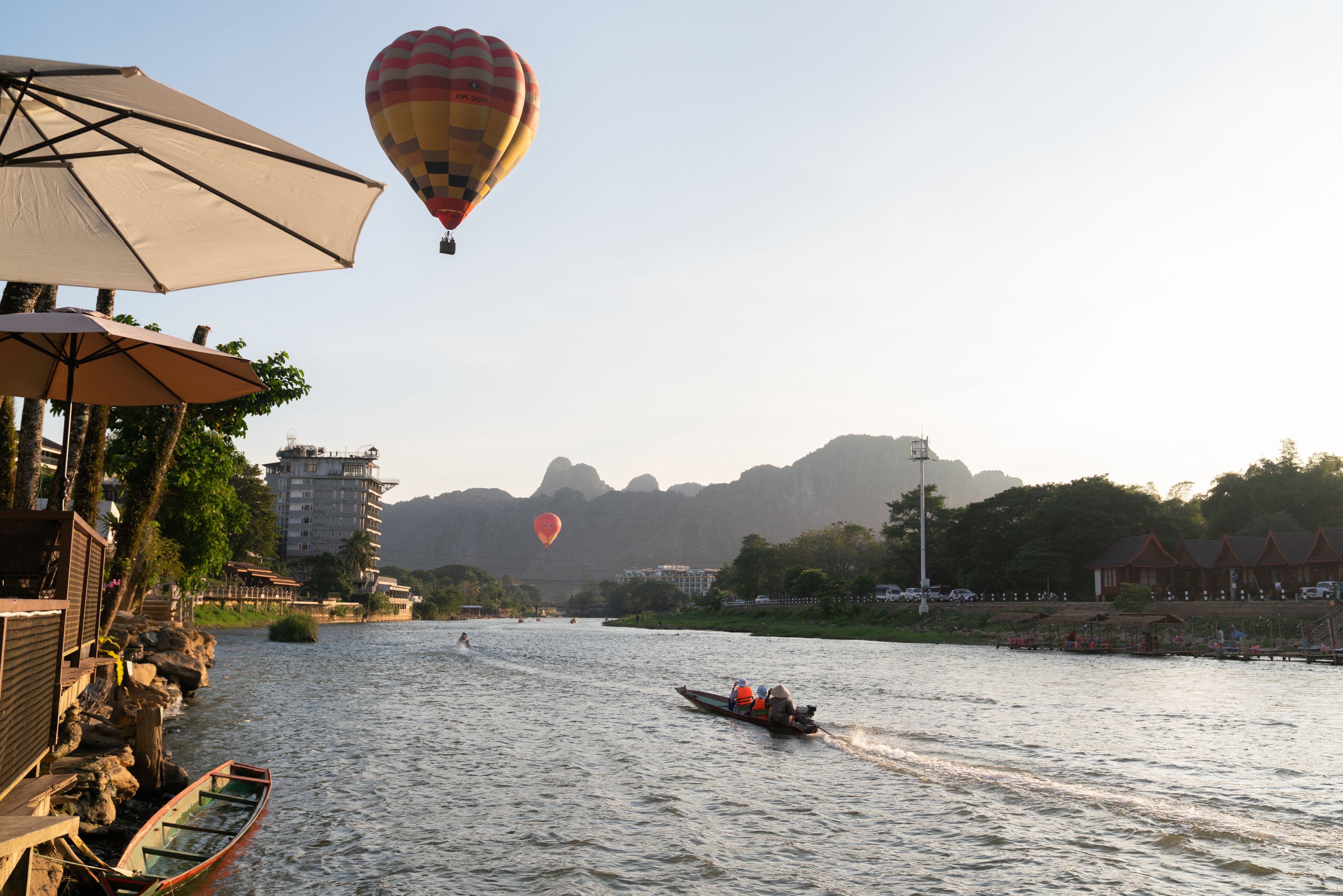 A hot-air balloon is seen in the sky as tourists travel in a boat along the Nam Song river in Vang Vieng on November 24, 2024. - The Laos government said on November 23 it was "profoundly saddened" by the deaths of foreign tourists in Vang Vieng, with the toll from a suspected methanol poisoning incident now at six. Six tourists died of suspected methanol poisoning after a night out in the Laos backpacker hotspot of Vang Vieng last week. (Photo by AFP)