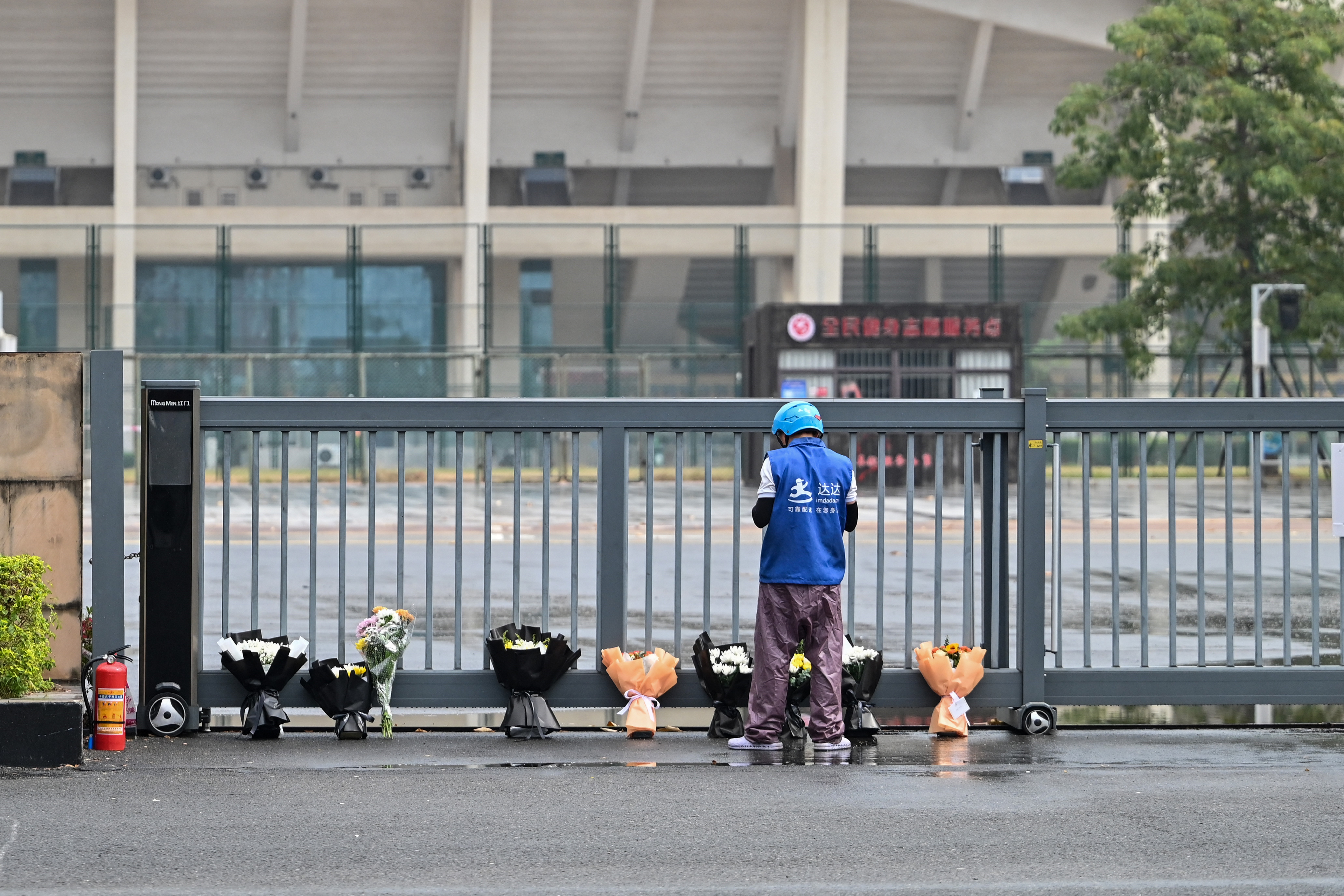 A delivery man lays online orders of flower bouquets at a makeshift memorial outside the Zhuhai Sports Centre in Zhuhai, in south China's Guangdong province on November 13, 2024 [Hector RETAMAL / AFP]