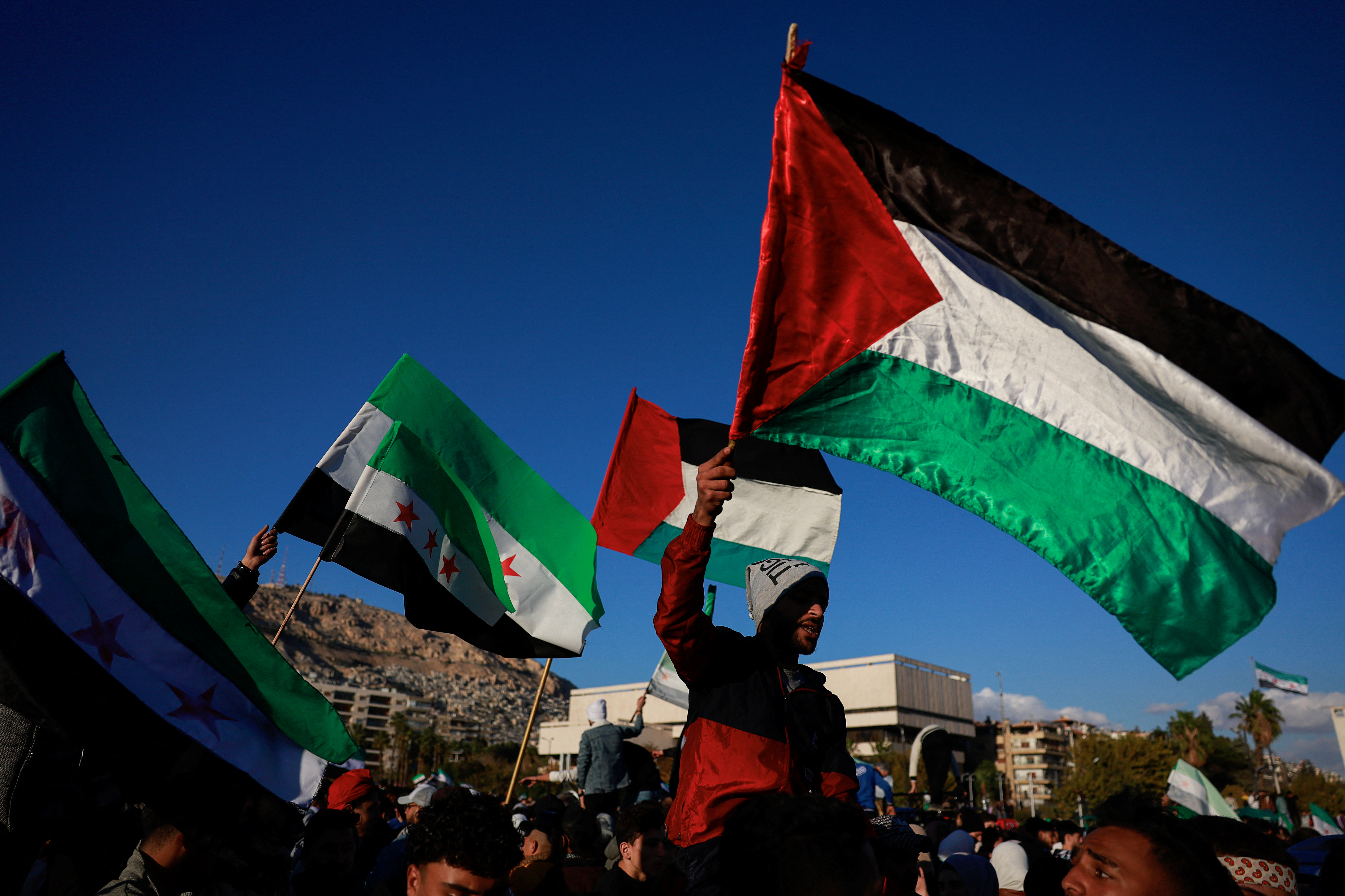 People wave the Palestinian flag and the flag adopted by the new Syrian rulers, as people celebrate after fighters of the ruling Syrian body ousted Syria's Bashar al-Assad, in the Damascus old city, Syria, December 13, 2024. REUTERS/Ammar Awad