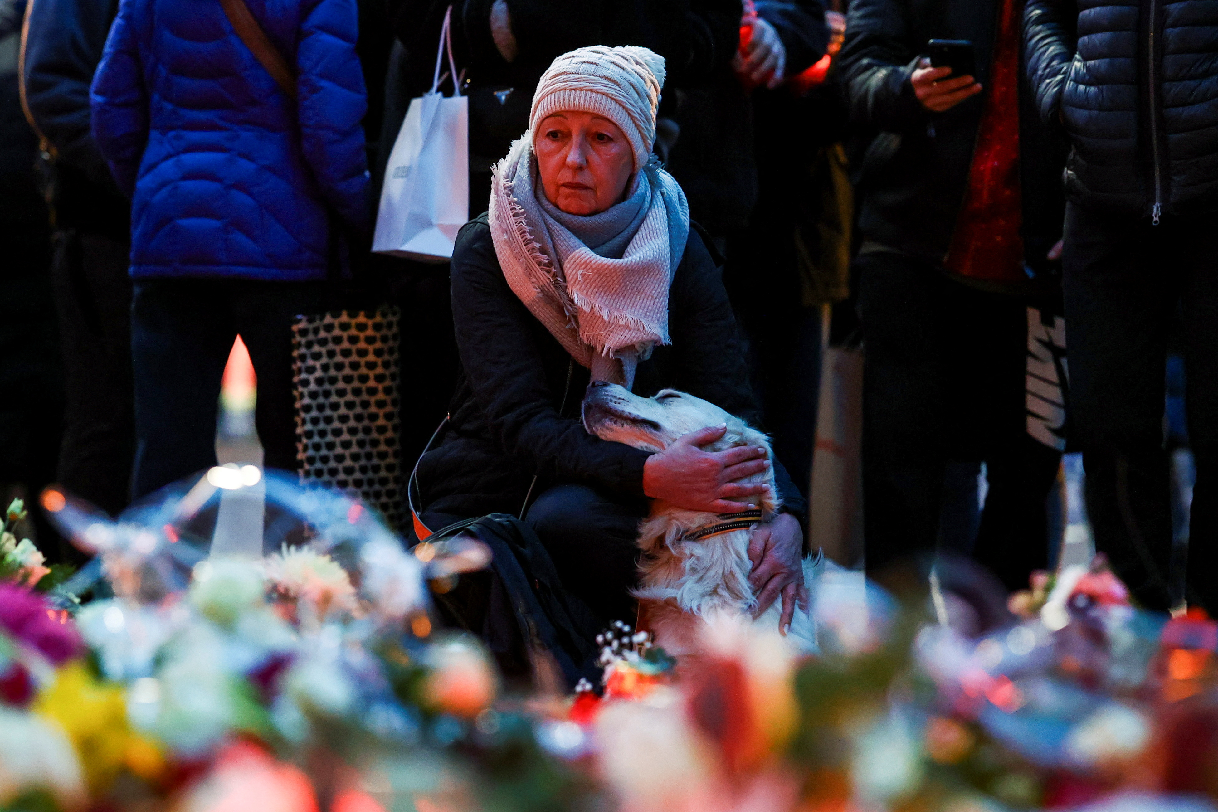 A woman pets a dog as people leave floral tributes to the victims near the site where a car rammed into a crowd at a Magdeburg Christmas market in Magdeburg, Germany December 21, 2024. REUTERS/Christian Mang TPX IMAGES OF THE DAY