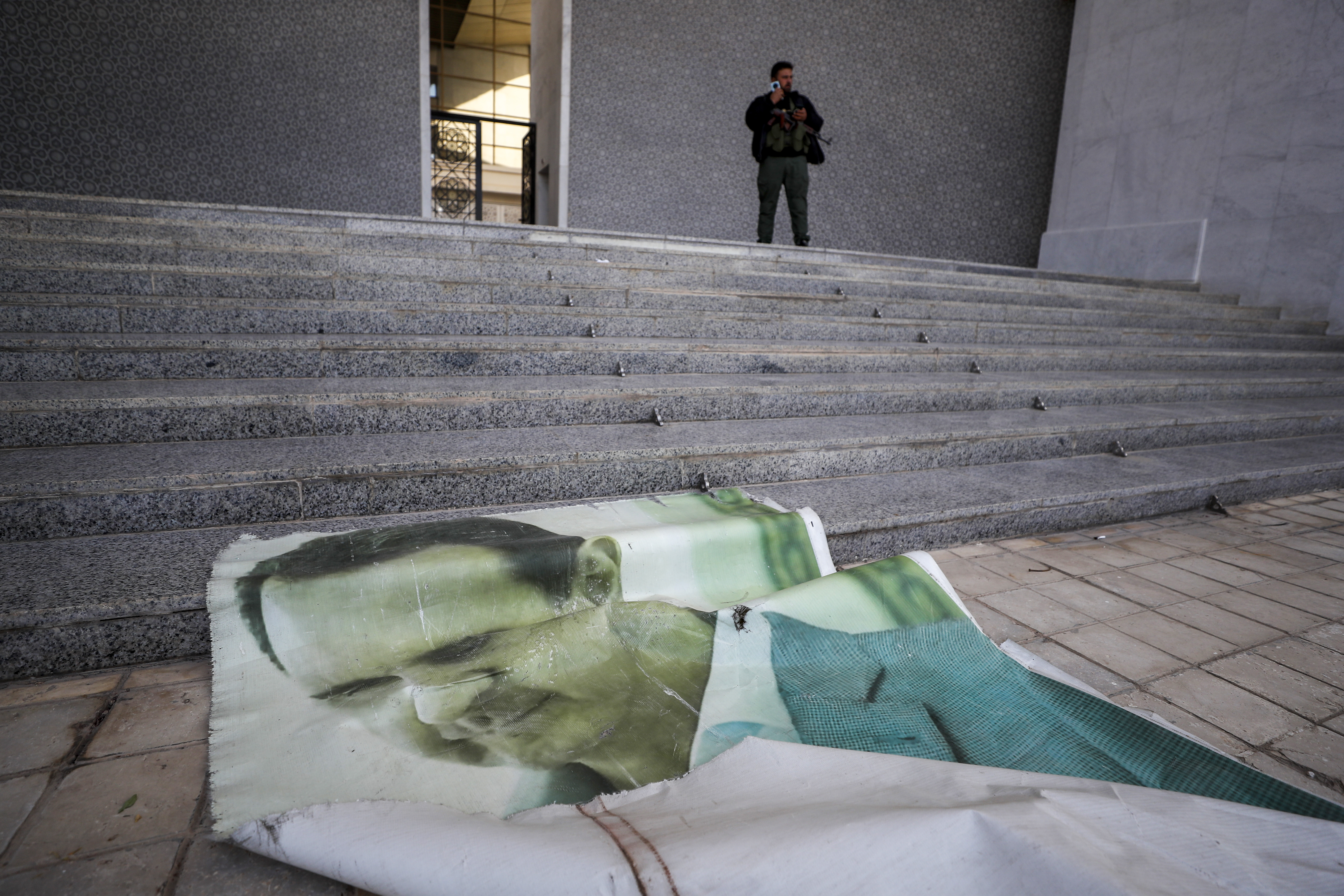 A giant picture of Syrian President Bashar Assad lies on the ground as a Syrian opposition fighter stands nearby, inside the Presidential Palace in Damascus, Syria