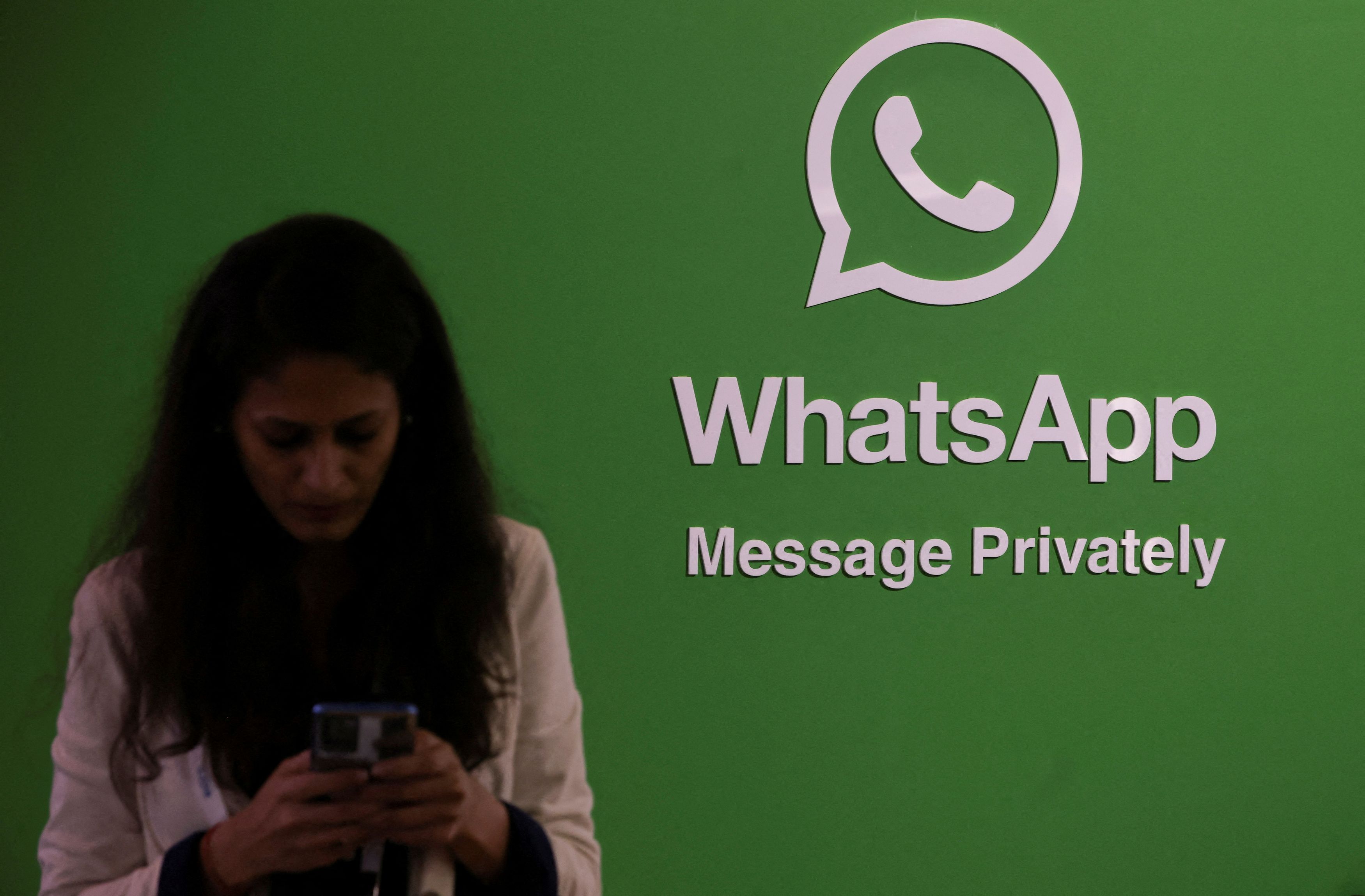 FILE PHOTO: A woman uses her phone next to a logo of the WhatsApp application [File: Francis Mascarenhas/Reuters]