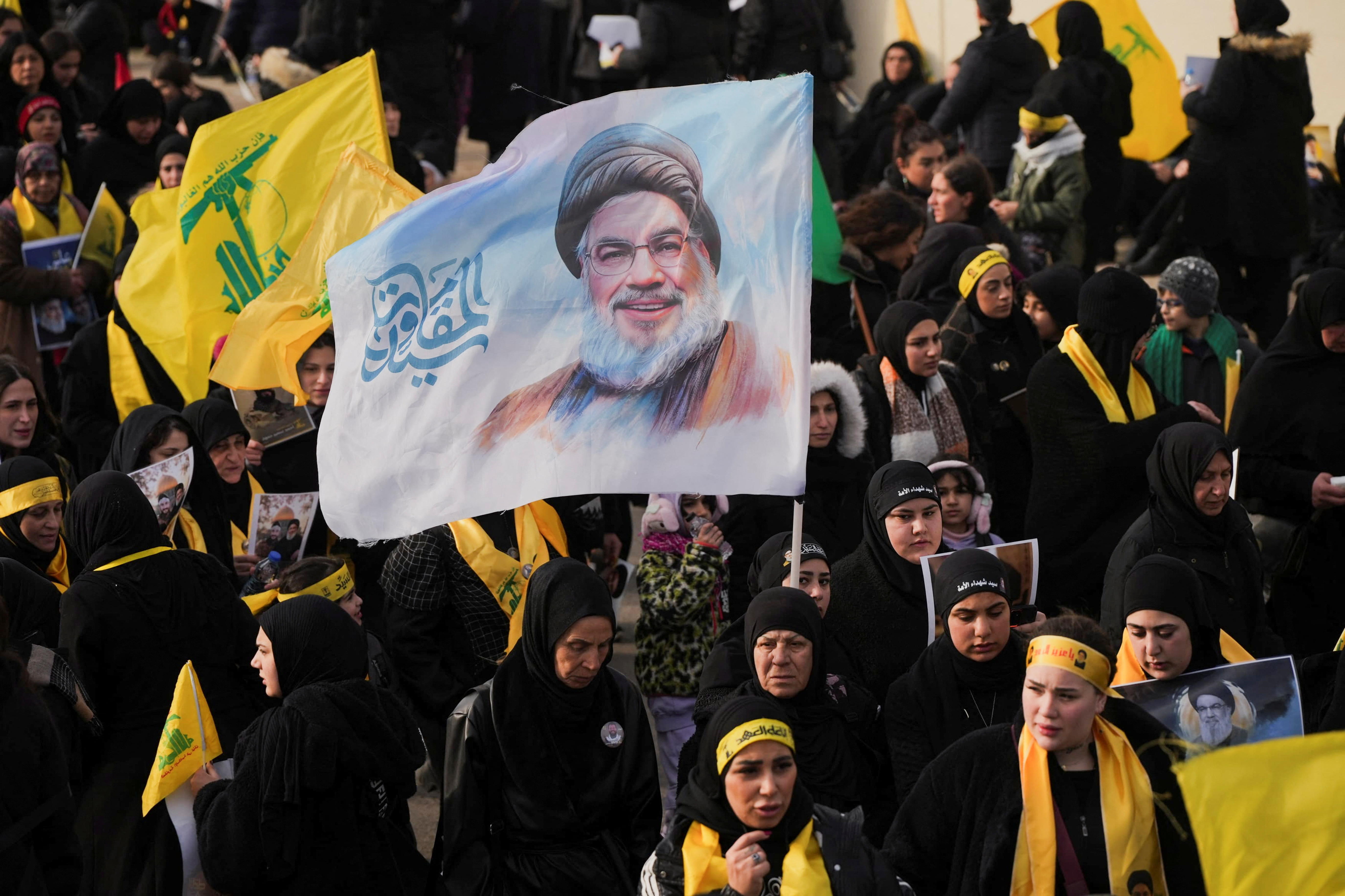 A person holds up a flag with a picture of the late Hezbollah leader Hassan Nasrallah