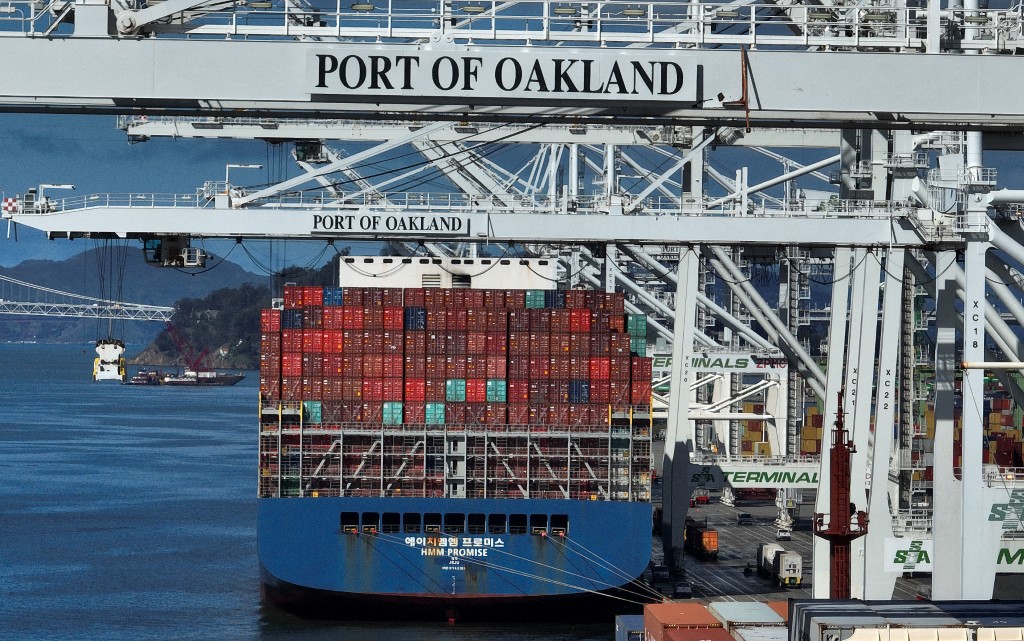 A shipping crane stands over a container ship at a port.