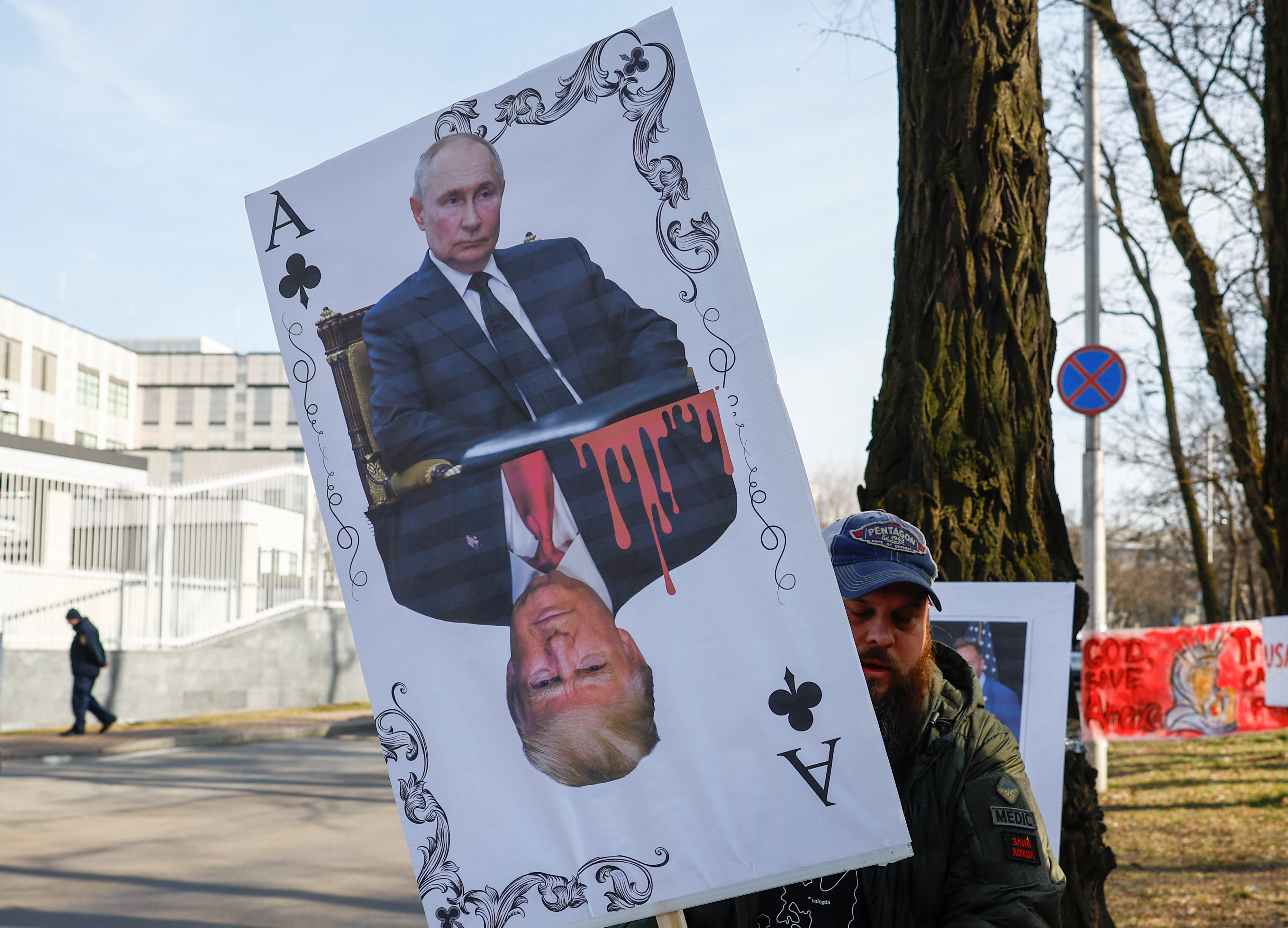 A demonstrator holds a banner depicting a playing card with portraits of Russian President Vladimir Putin and US President Donald Trump [File: Valentyn Ogirenko/Reuters]