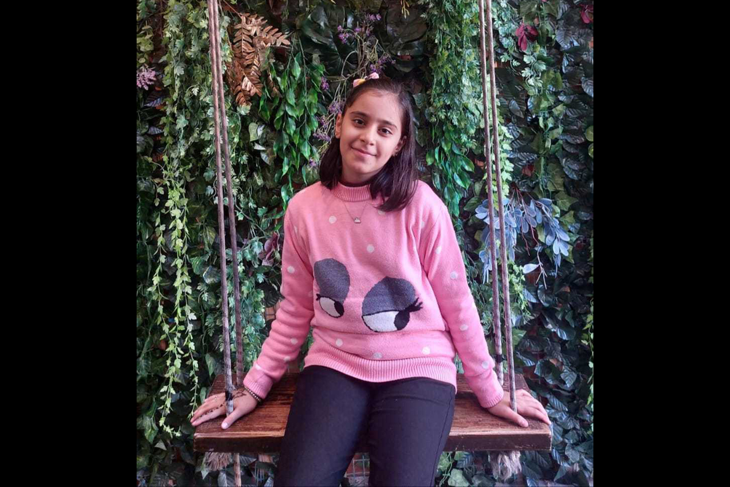A little girl in a pink sweater on a rope swing, with a sweet smile on her face