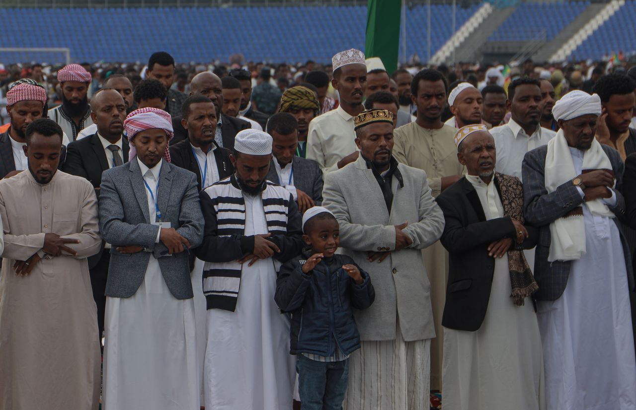 Rows of Ethipian men praying, with a smiling little boy in the front row