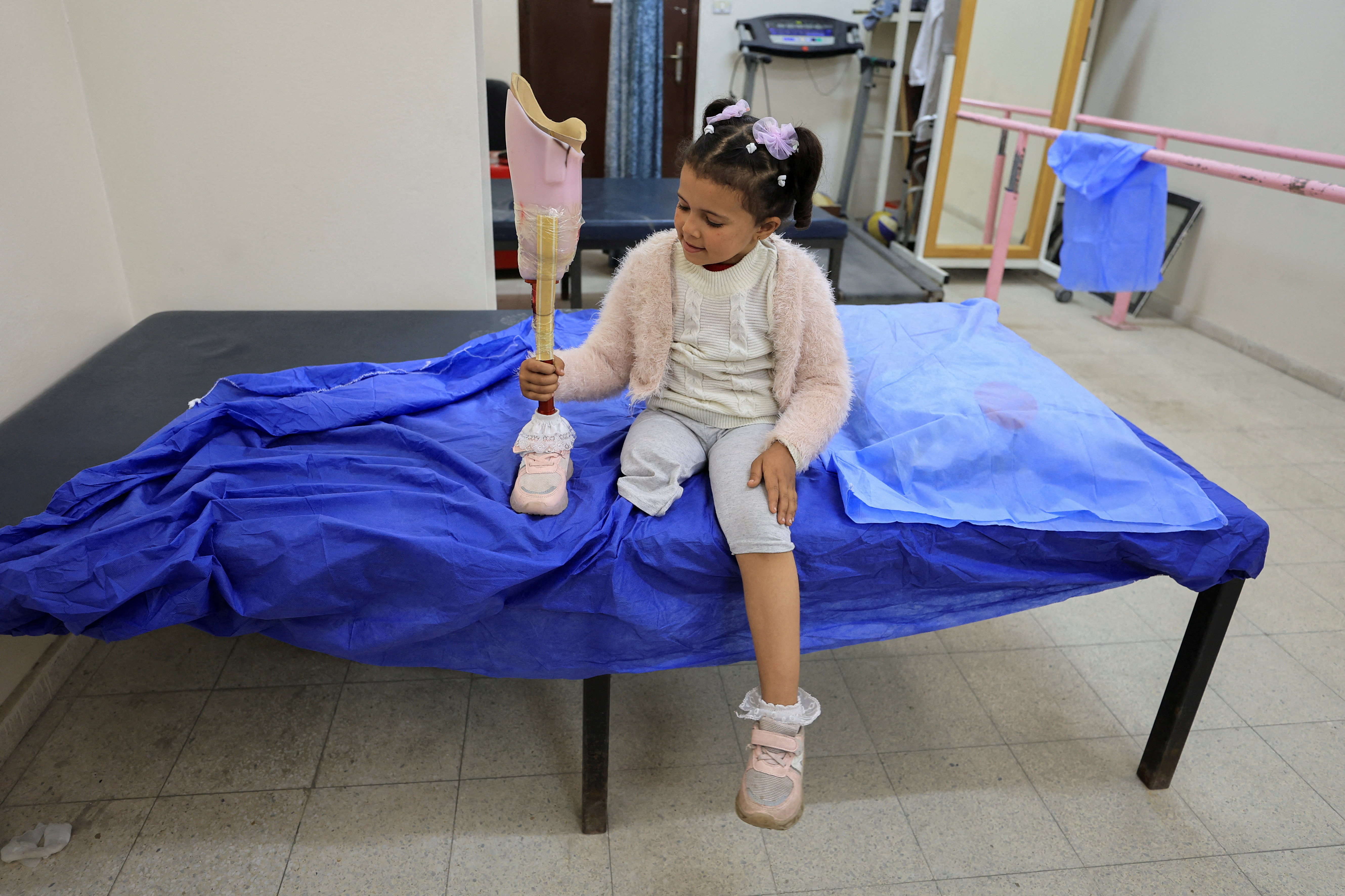 A girl holds her artificial leg on a hospital bed