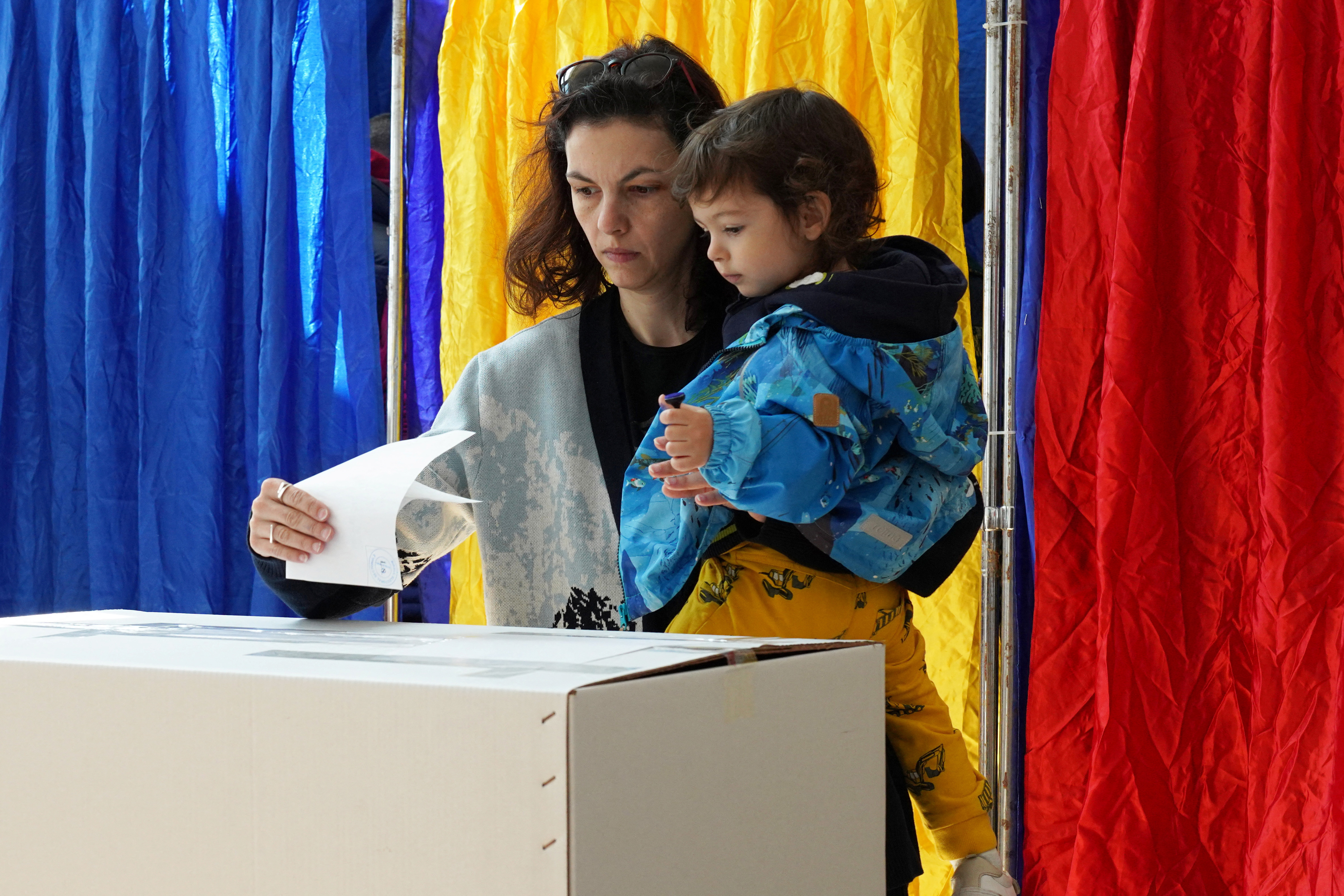 A woman holds a child as she votes, during Romania's second round of the presidential election