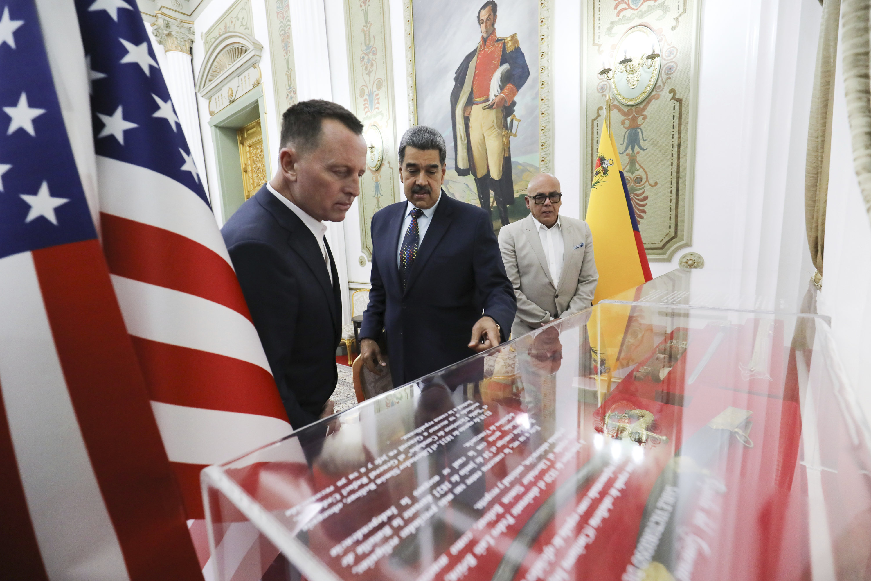 Richard Grenell and Nicolas Maduro look at a glass case in Caracas, between US flags
