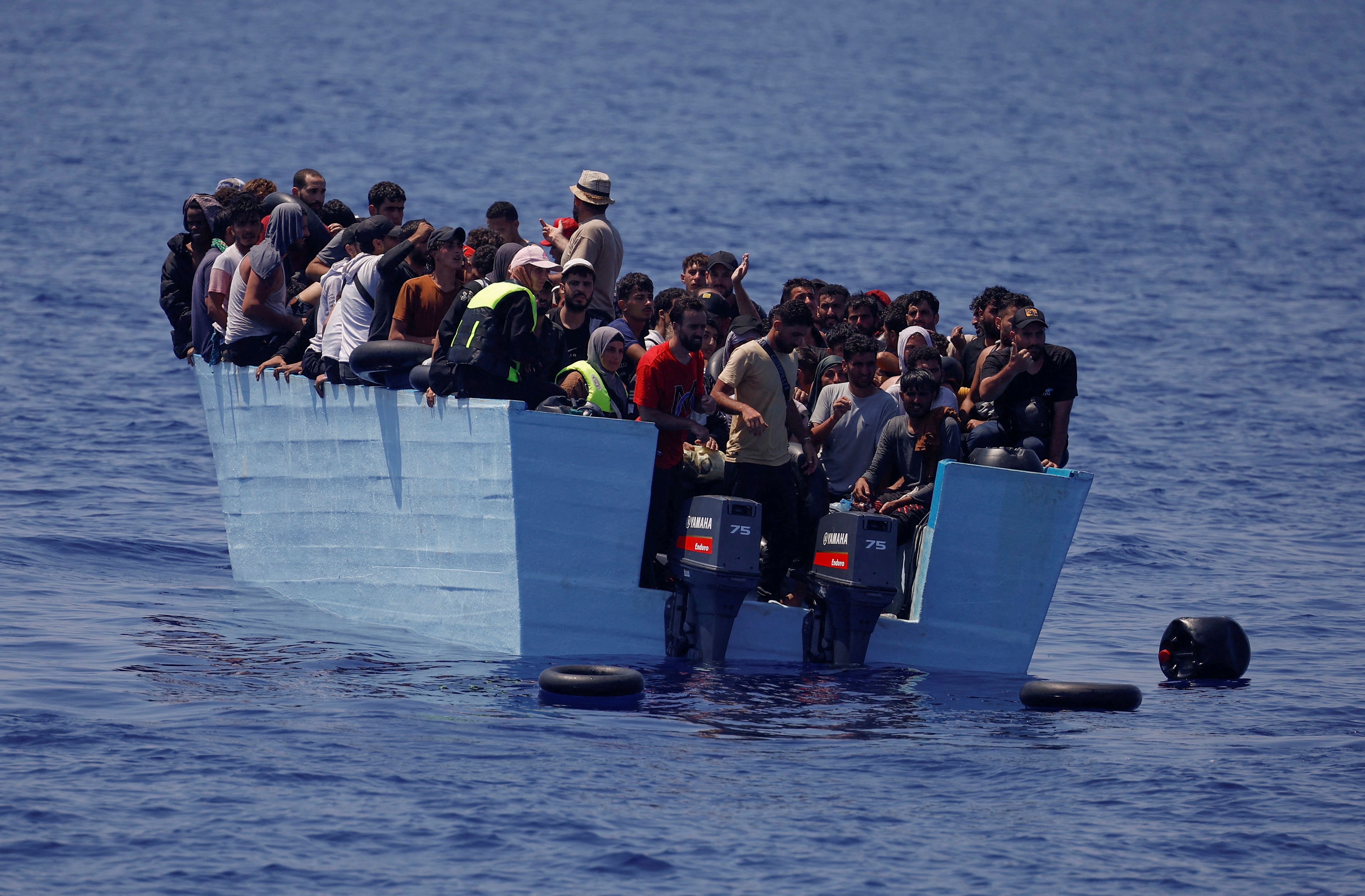 Refugees and migrants stand on a wooden boat near NGO Open Arms rescue boat